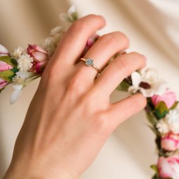 BlackLine Photo Damian Kasperowicz - Dłoń z pierścionkiem zaręczynowym na tle kwiatowego wianka w Białymstoku. Delikatne oświetlenie podkreśla detale biżuterii i tatuaż na nadgarstku.