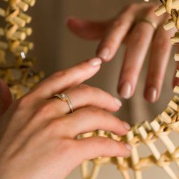 BlackLine Photo Damian Kasperowicz - Delikatny pierścionek zaręczynowy na kobiecej dłoni, odbity w wiklinowym lustrze. Subtelny manicure nude. Ciepłe oświetlenie podkreśla blask złota i diamentów.