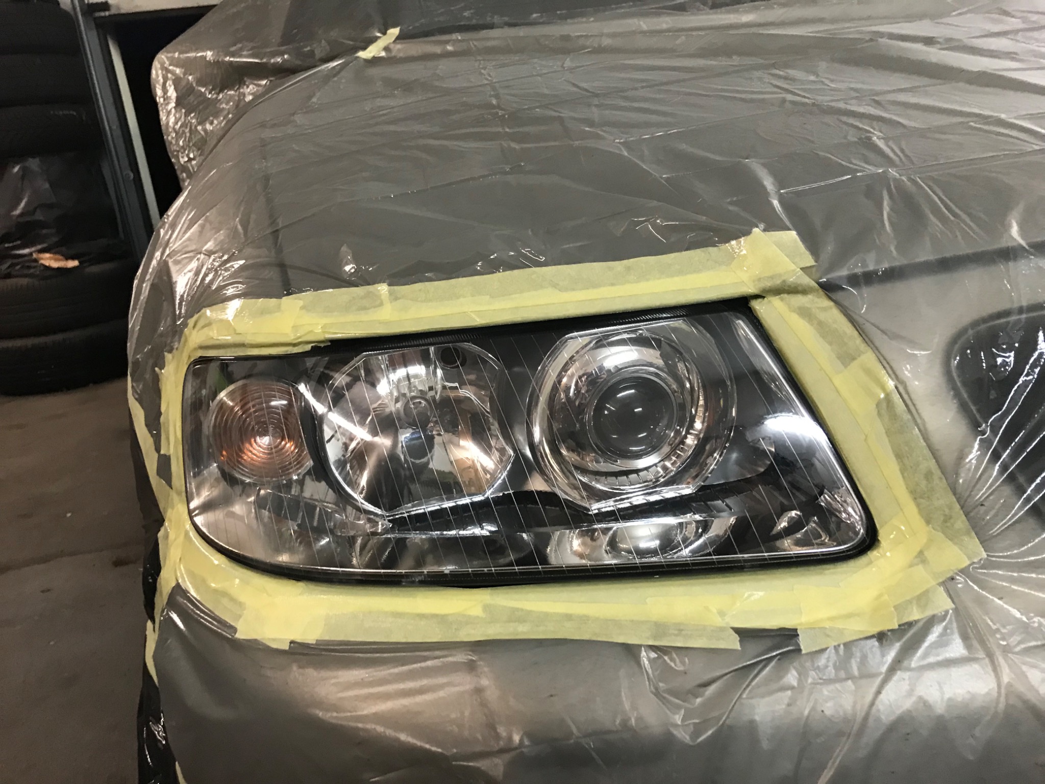 Przygotowanie samochodu do naprawy lakierniczej: reflektor zabezpieczony taśmą malarską i folią ochronną.