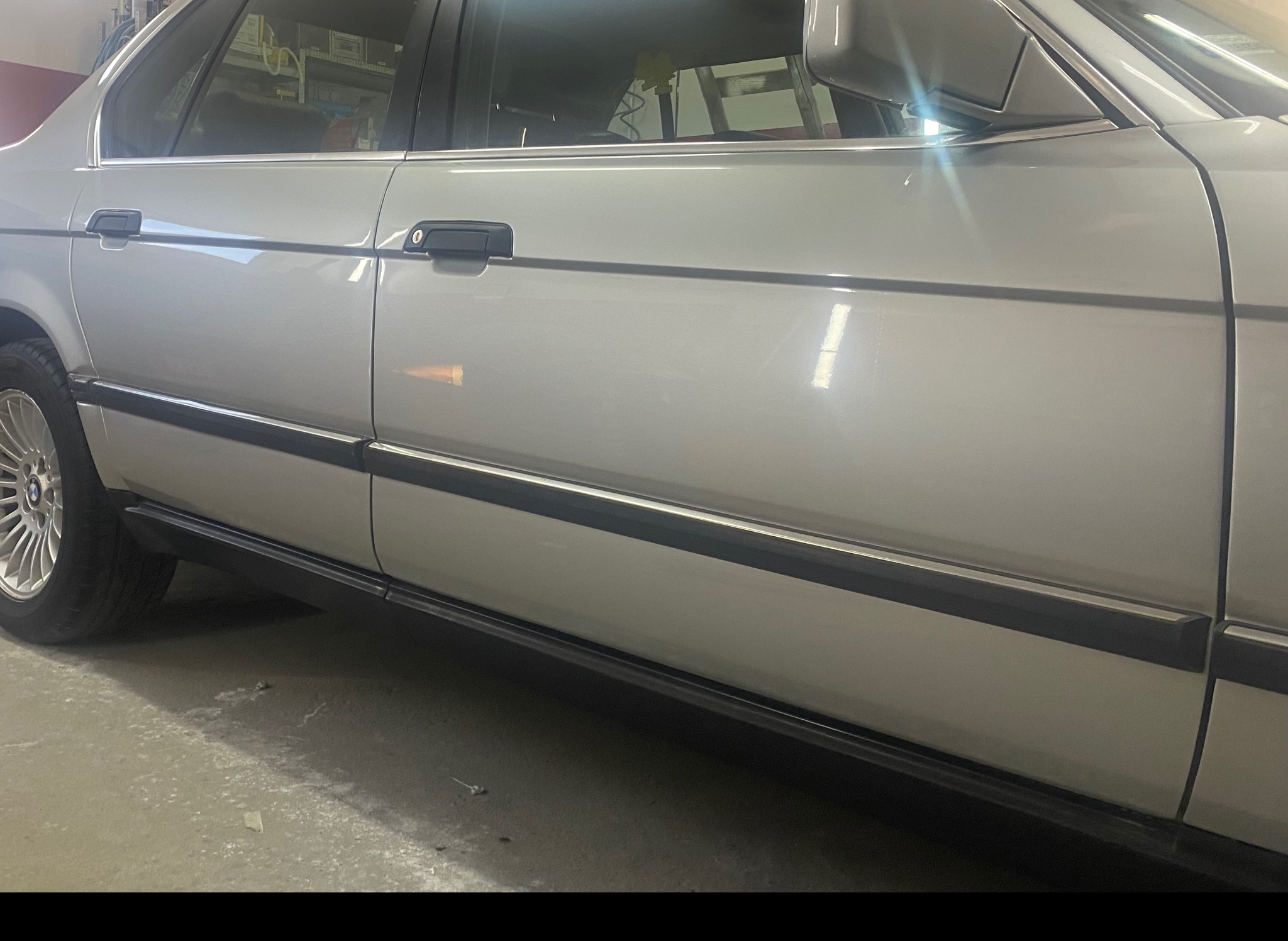 Boczny widok srebrnego sedana BMW E32 po renowacji lakieru, z widocznymi detalami karoserii i aluminiowymi felgami.