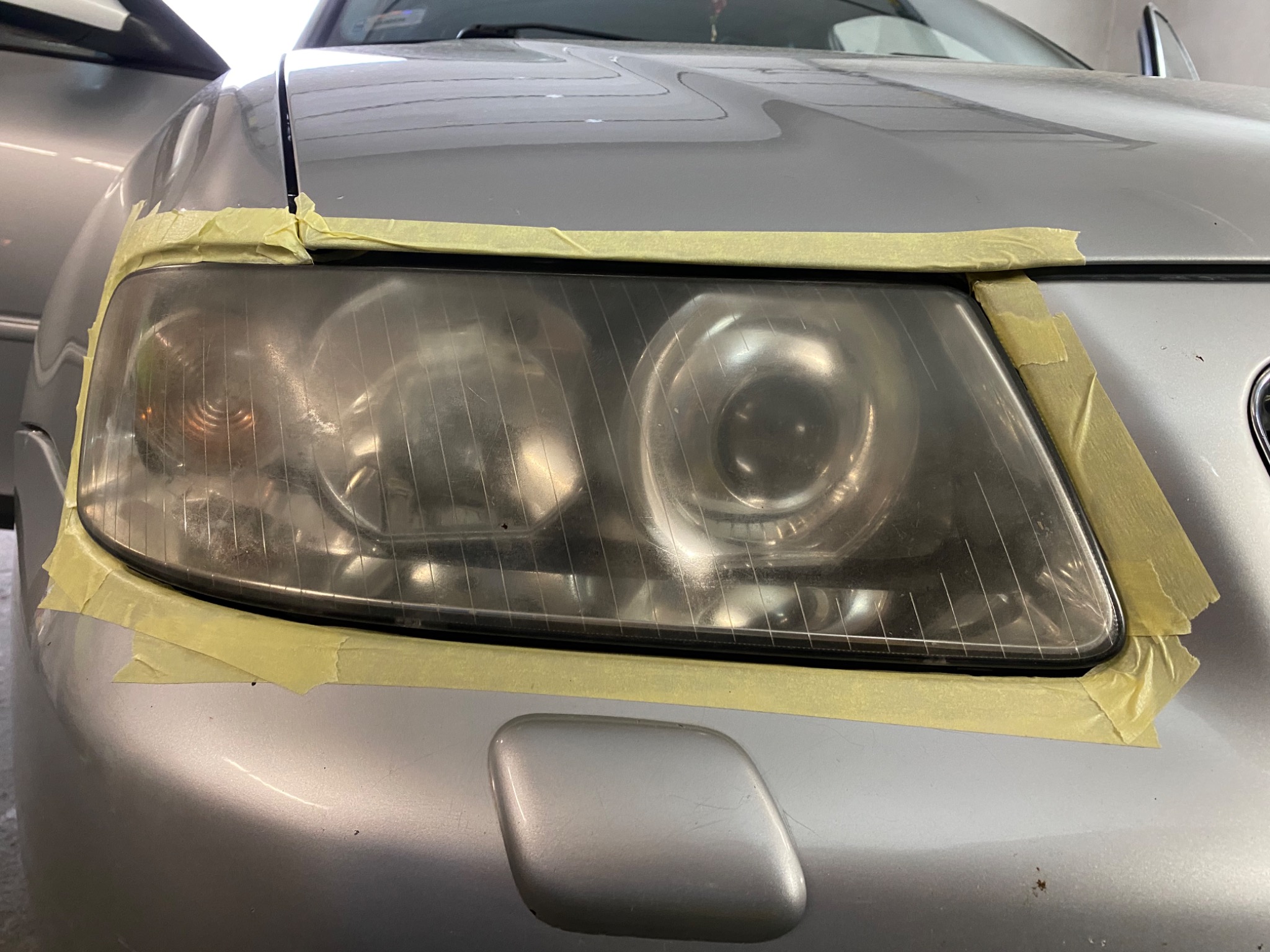Przygotowanie reflektora srebrnego samochodu do polerowania, zabezpieczonego taśmą malarską.