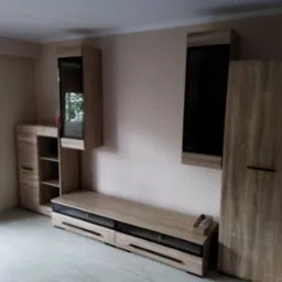 Zmontowany zestaw mebli do salonu w odcieniach drewna z czarnymi akcentami, składający się z szafek wiszących, szafki RTV i wysokiej szafy, ustawiony na jasnej podłodze.