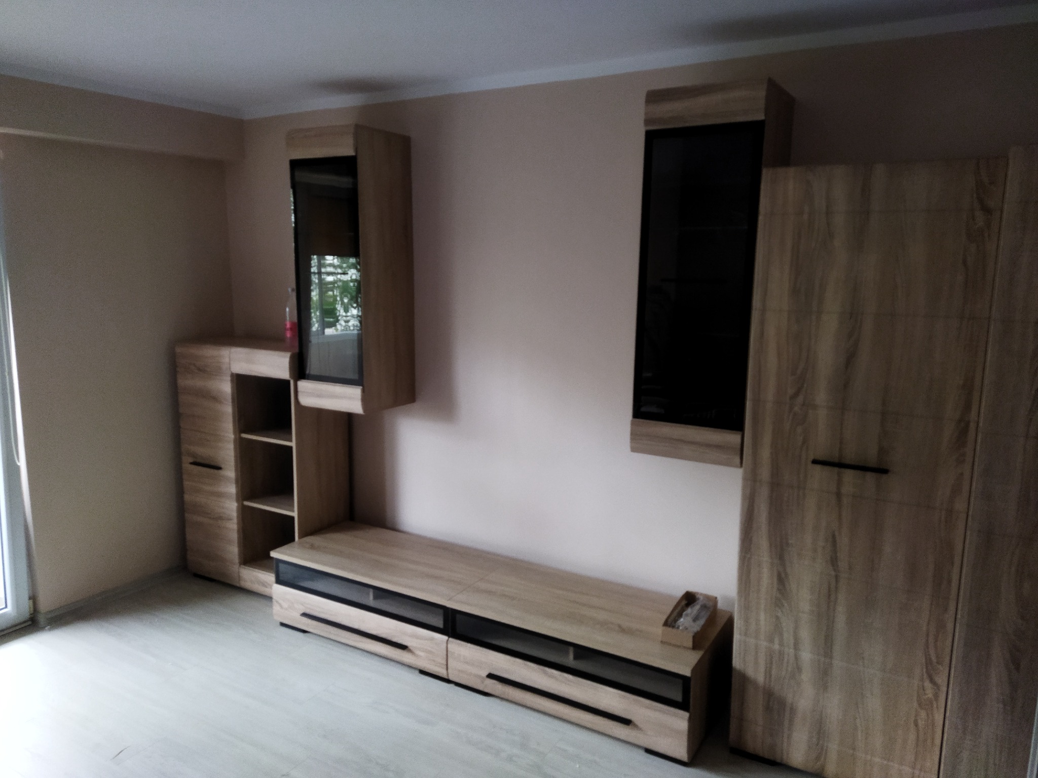 Zmontowany zestaw mebli do salonu w odcieniach drewna z czarnymi akcentami, składający się z szafek wiszących, szafki RTV i wysokiej szafy, ustawiony na jasnej podłodze.