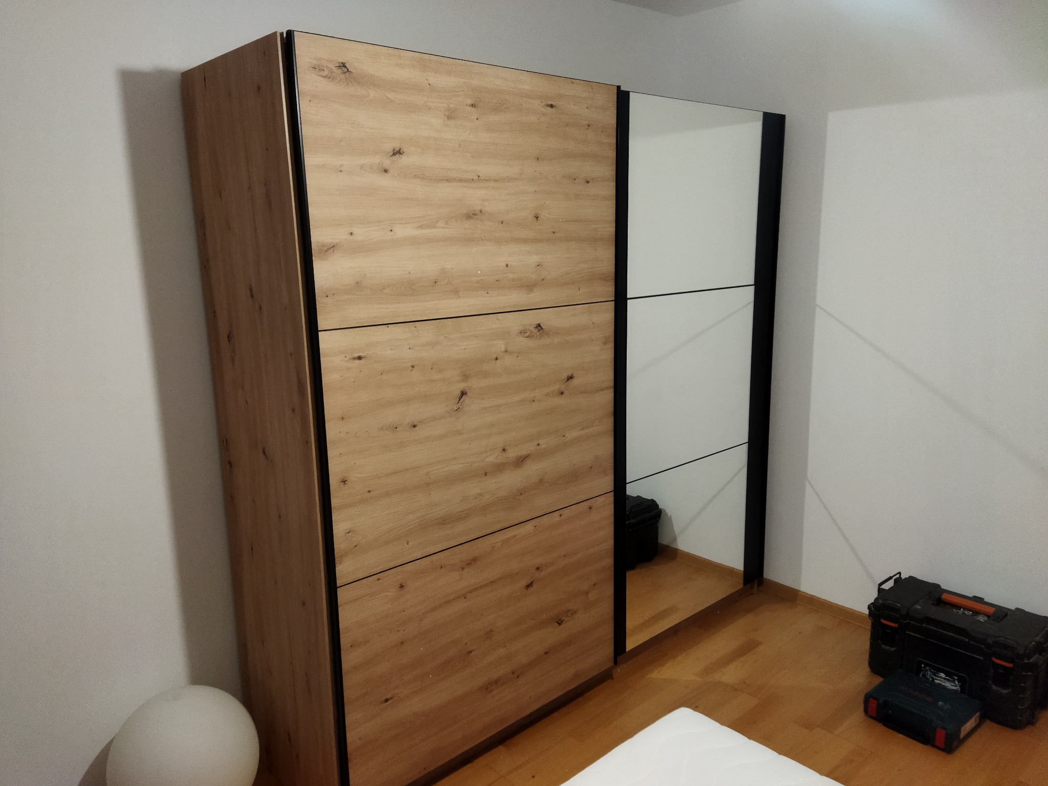 Szafa przesuwna z drewnopodobnymi frontami i lustrzanymi drzwiami, obok widoczne skrzynki z narzędziami.