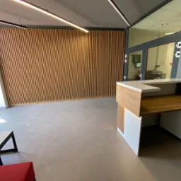 Nowoczesne biuro z drewnianą ścianą z pionowych paneli, recepcją z blatem w kolorze drewna i białymi szafkami, jasną podłogą i oświetleniem LED.