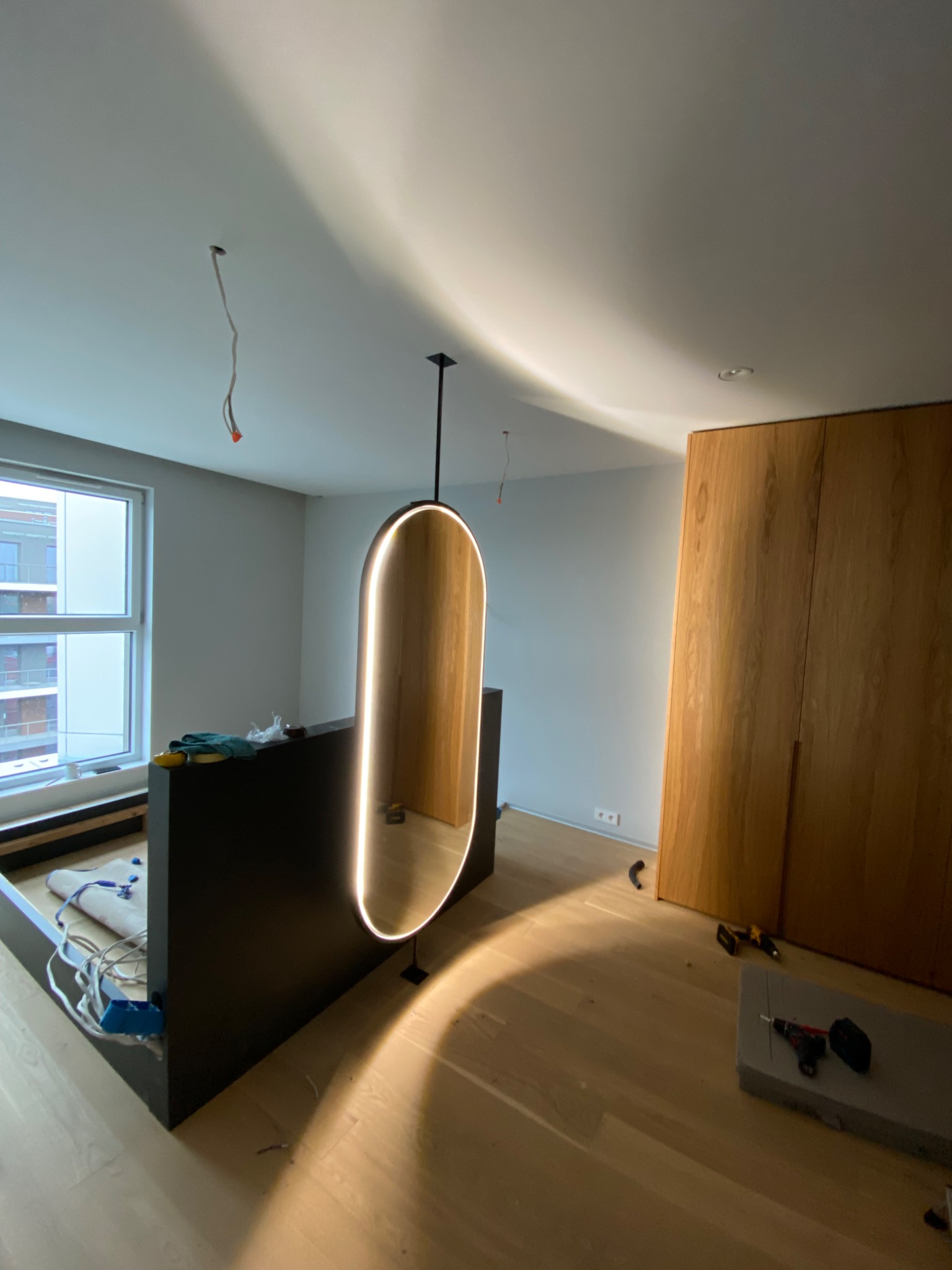 Nowoczesna antresola z podświetlanym, owalnym przejściem i drewnianą zabudową ścienną w trakcie montażu, narzędzia na podłodze.