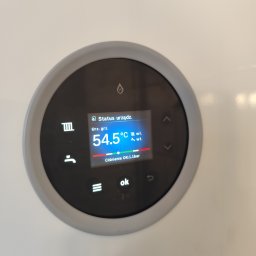 Panel sterowania kotła gazowego z wyświetlaczem wskazującym temperaturę 54.5°C i ciśnienie 1.1 bar. Widoczne ikony grzania i ciepłej wody użytkowej.