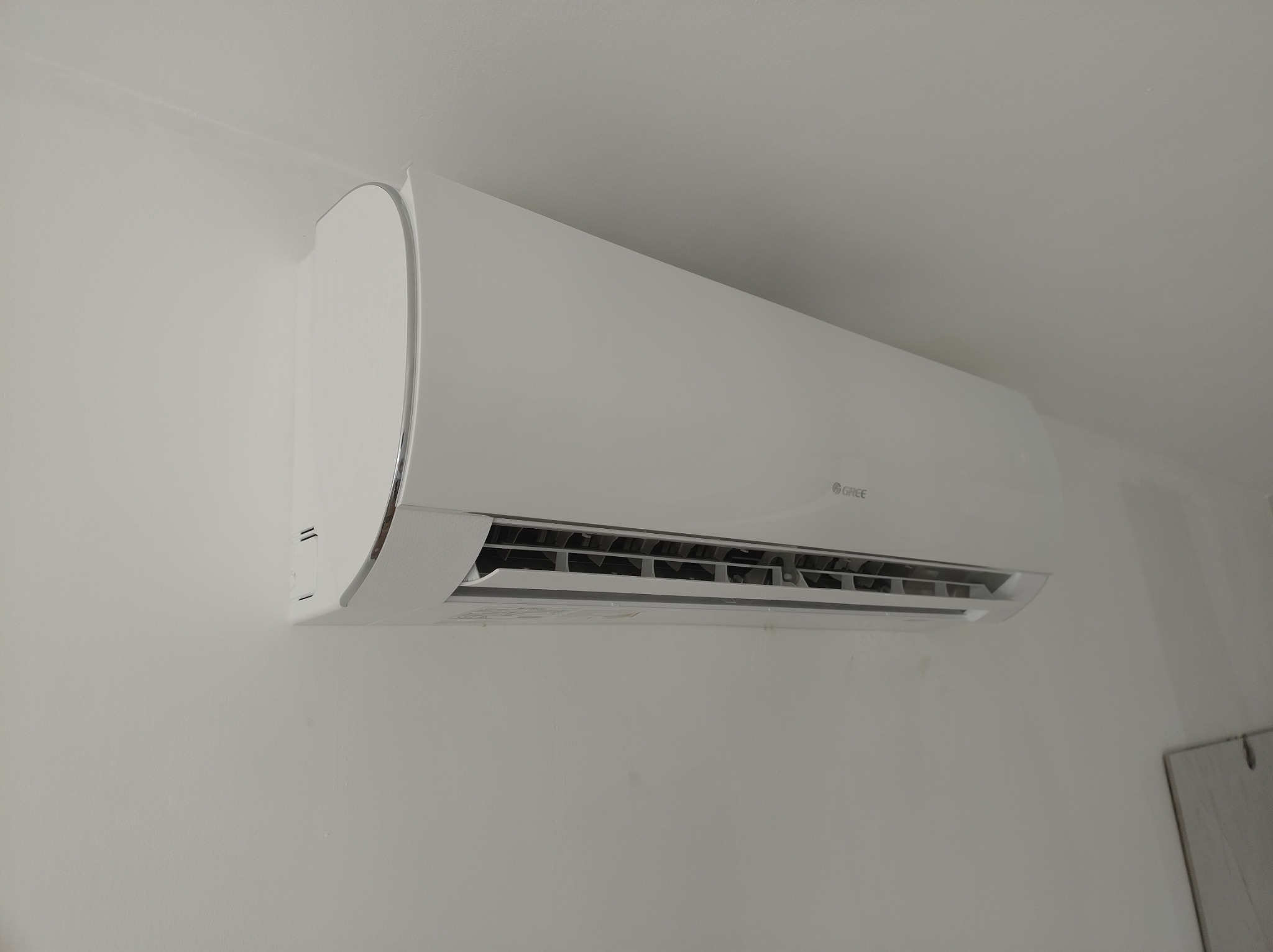 Biała jednostka wewnętrzna klimatyzatora marki Gree, zamontowana na jasnej ścianie w pomieszczeniu.