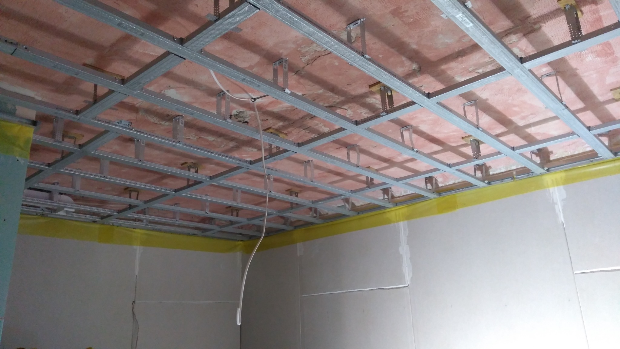 Stelaż metalowy sufitu podwieszanego z płyt karton gips, widoczna instalacja elektryczna i zabezpieczona folią ściana