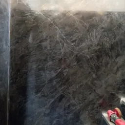 Ściana z efektem dekoracyjnym w odcieniach szarości, imitująca kamień. Widoczne narzędzie do polerowania na schodach. Unikalna faktura i oświetlenie podkreślają głębię.