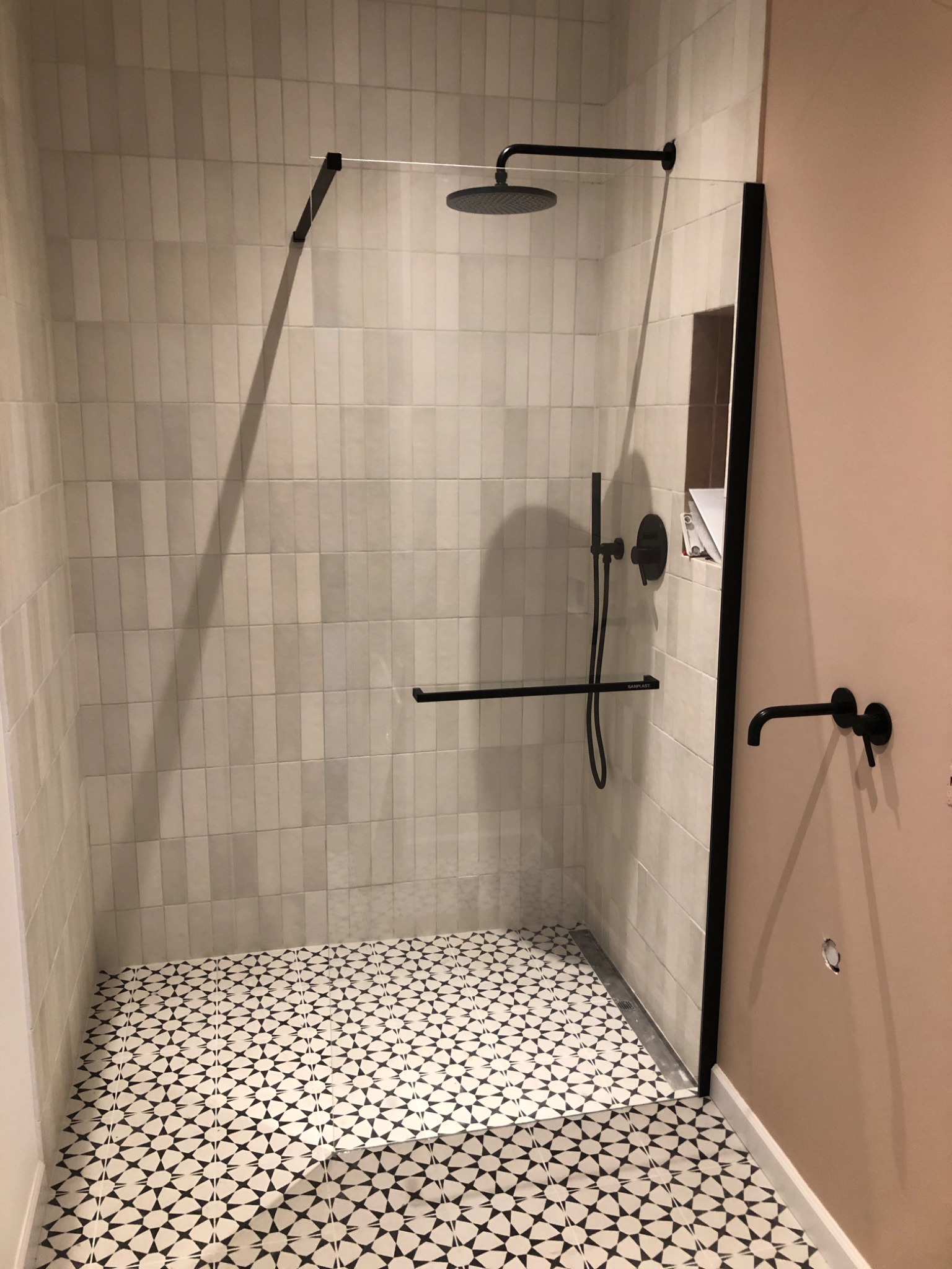 Nowoczesna kabina prysznicowa z czarną armaturą, jasnymi płytkami wertykalnymi i wzorzystą podłogą.