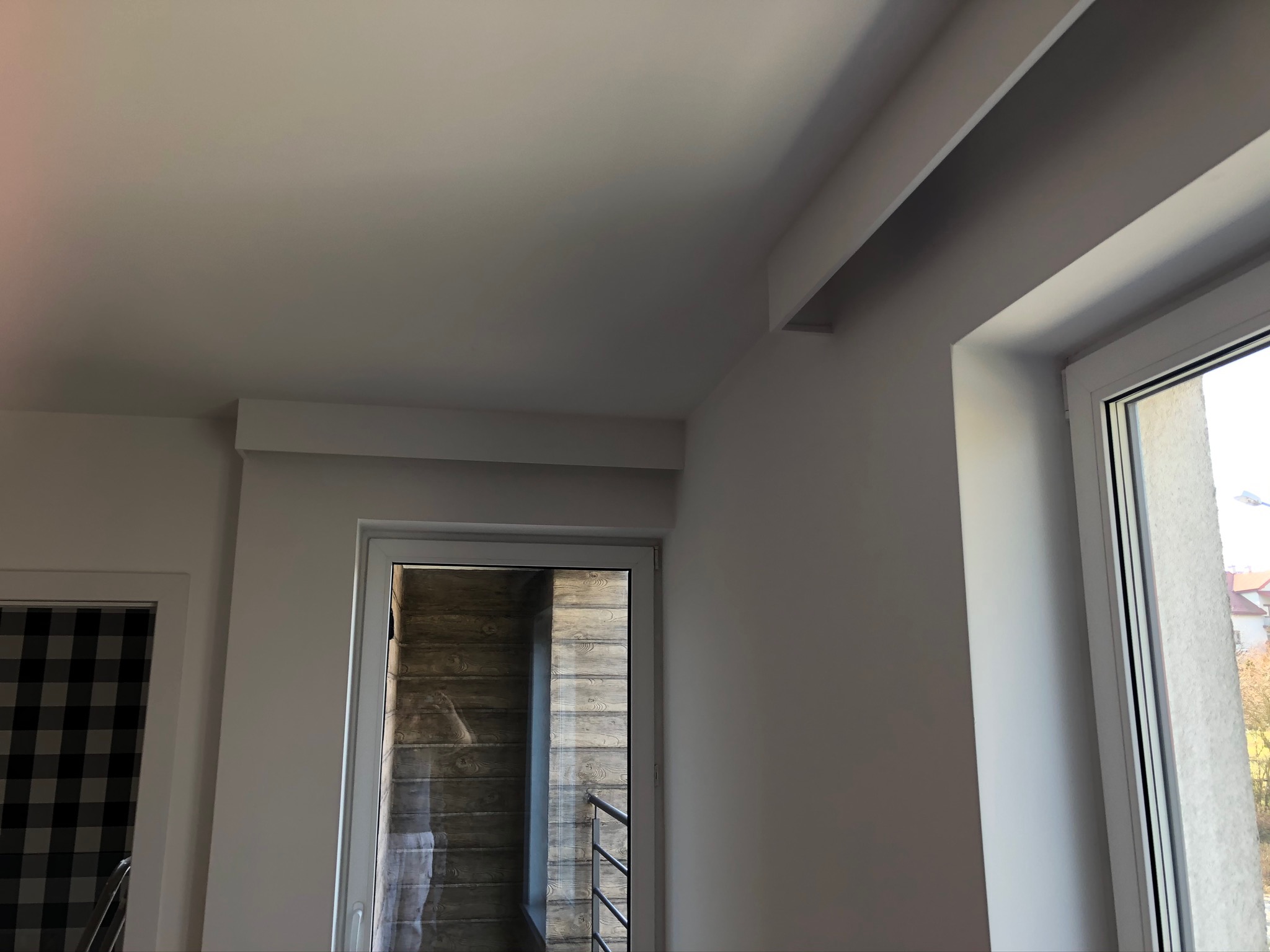 Białe wnętrze po remoncie z widocznymi sufitami, oknem i drzwiami balkonowymi z drewnianą okładziną.