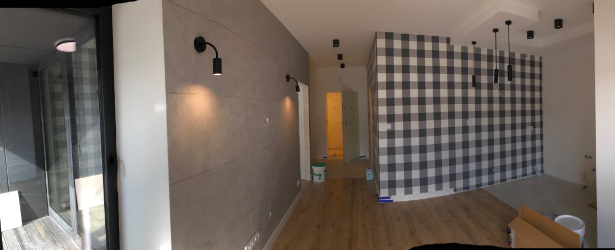 Wnętrze pokoju po odświeżeniu: ściana z efektem betonu oświetlona kinkietami, ściana w biało-szarą kratę, drewniana podłoga, widoczne akcesoria malarskie.