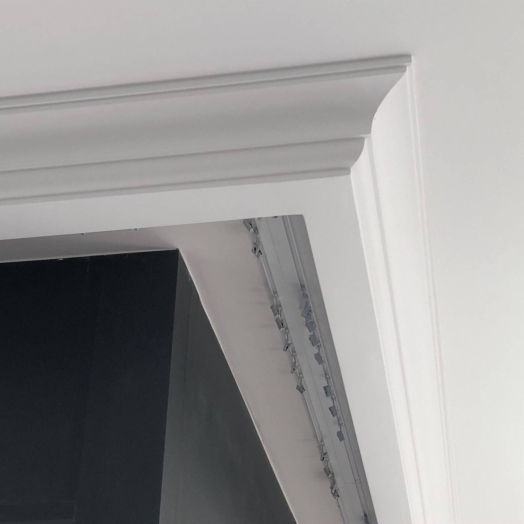 Detail of newly installed white decorative molding above a doorway, showing unfinished edges and metal fasteners.