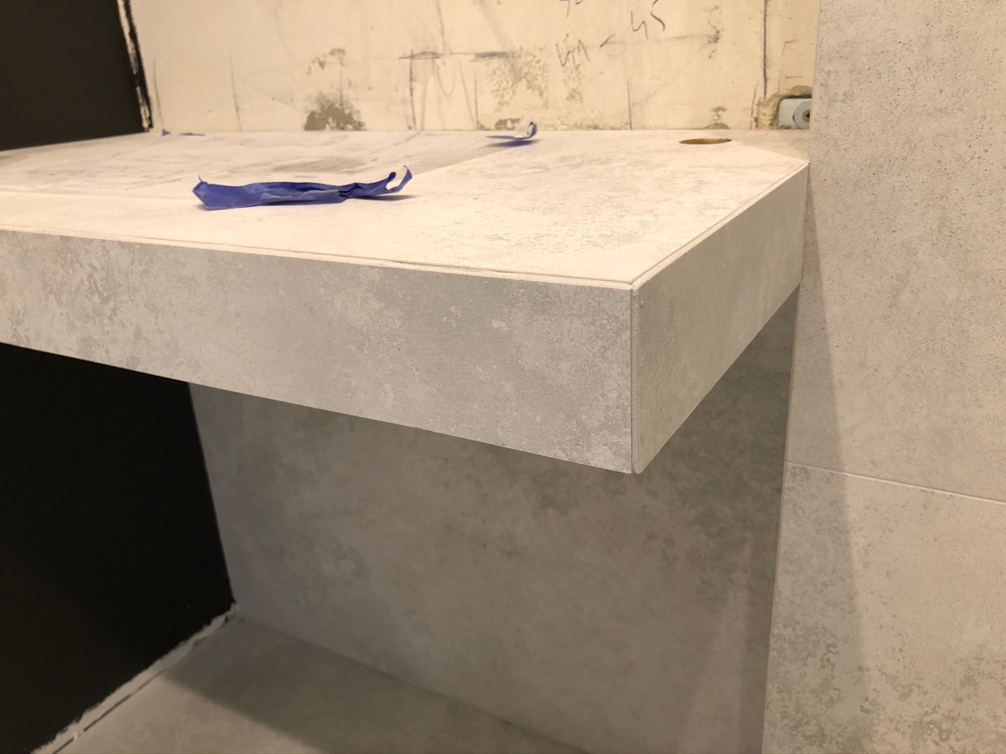 Montaż blatu z płytek ceramicznych w łazience, widoczne fragmenty nieotynkowanej ściany i niebieska taśma zabezpieczająca.