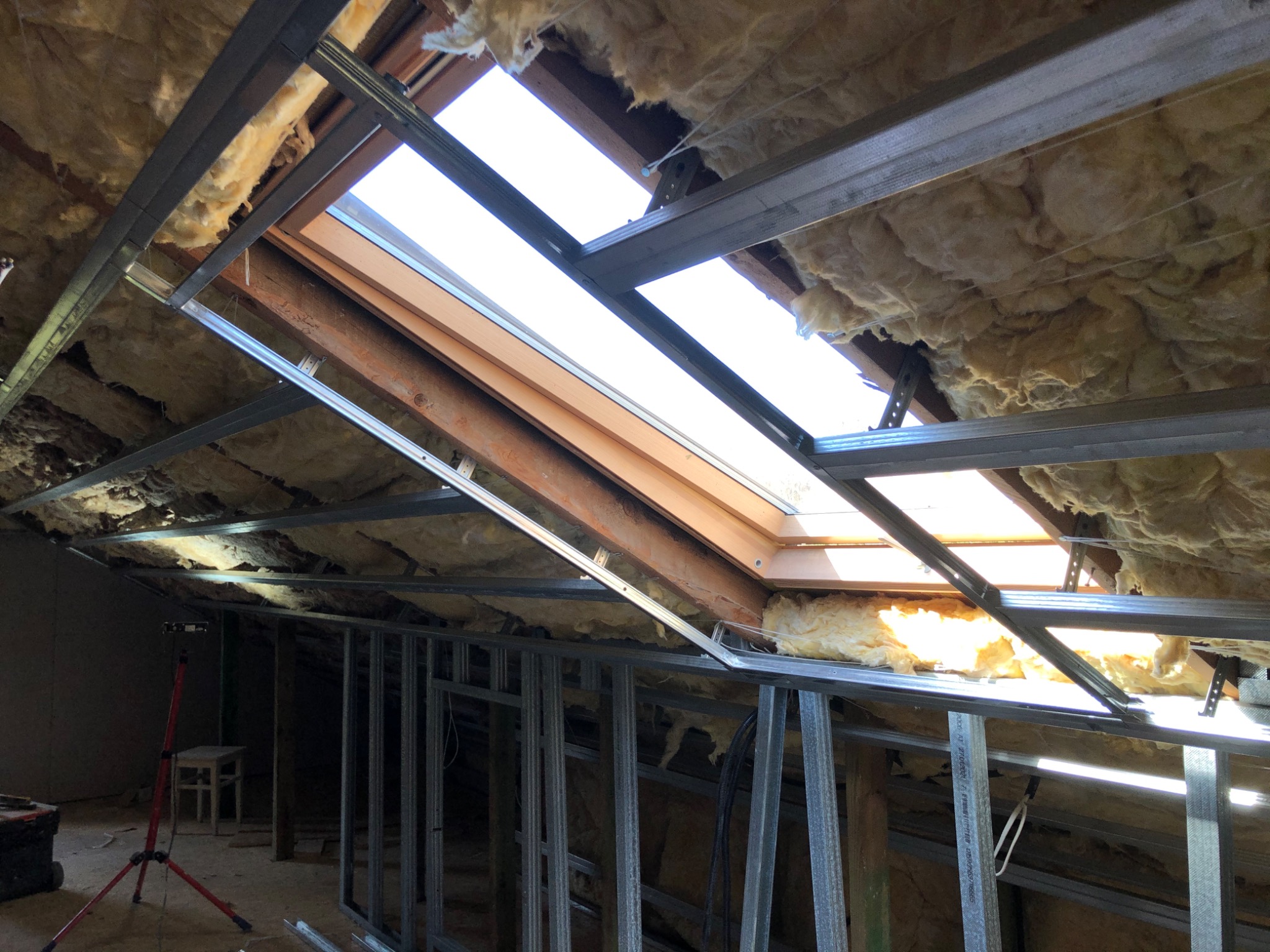 Poddasze w trakcie ocieplania z widoczną konstrukcją metalową pod płyty gipsowo-kartonowe, izolacją z wełny mineralnej oraz oknami dachowymi.