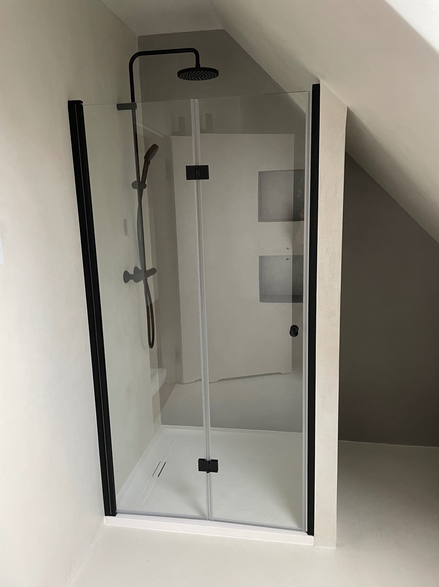 Kabina prysznicowa z czarnymi profilami w łazience na poddaszu, widoczna deszczownica i bateria prysznicowa.