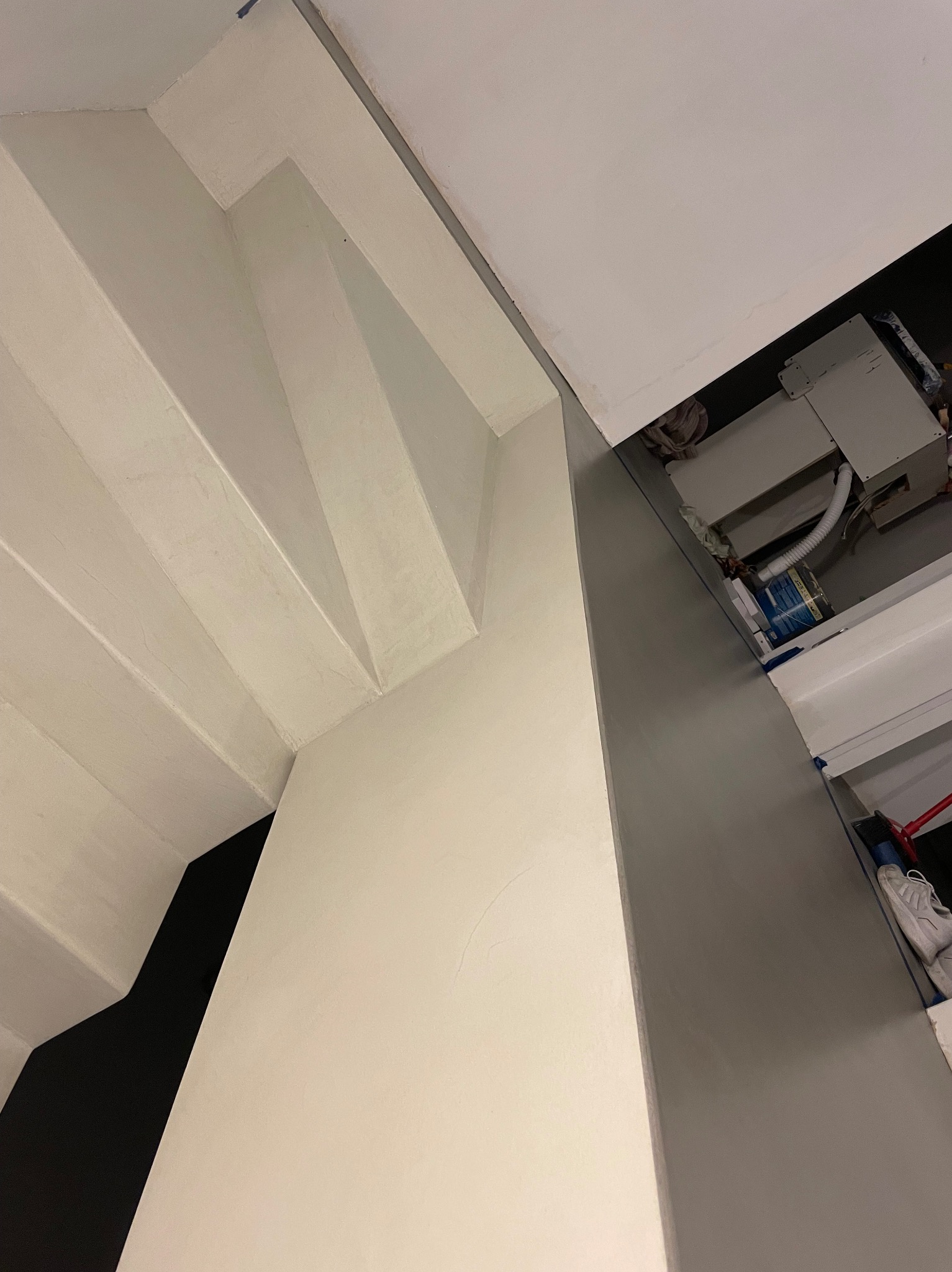 Szare wykończenie ściany z widocznymi schodami w tle, ujęcie z dołu ukazujące minimalistyczny design.