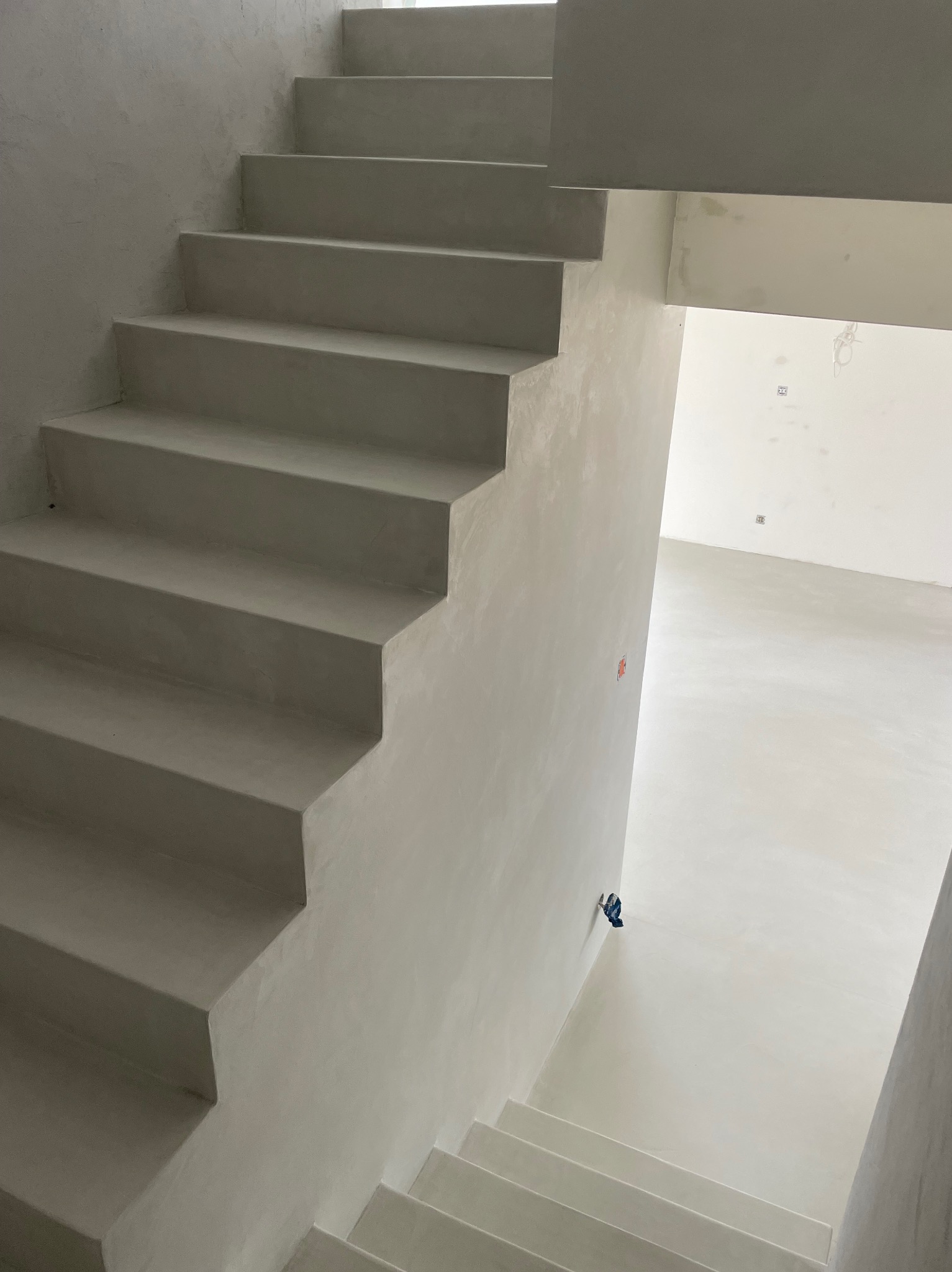 Minimalistyczne schody i posadzka pokryte jednolitą, jasnoszarą powłoką, widok z góry, surowe wykończenie wnętrza w trakcie remontu.