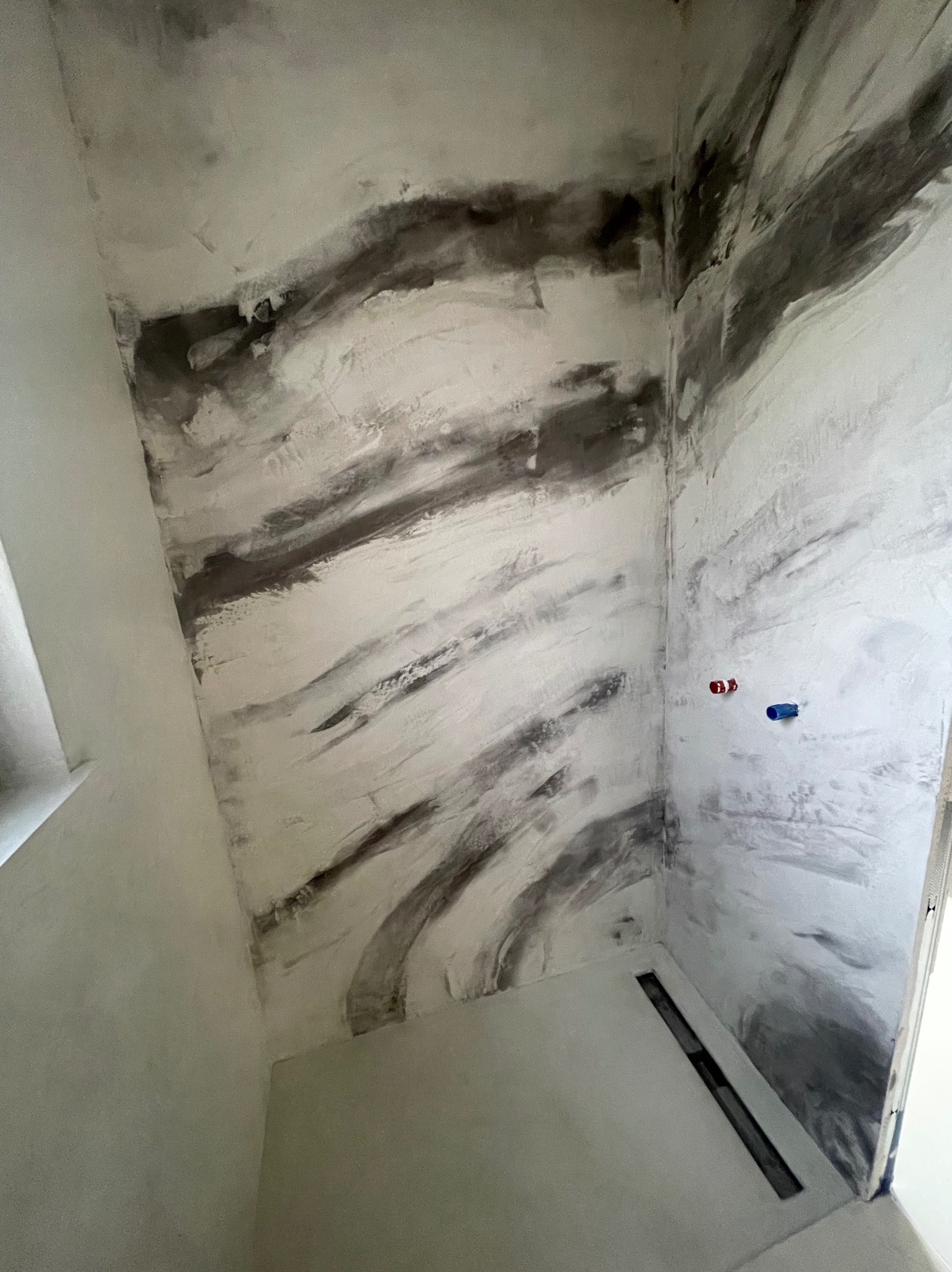 Wnętrze łazienki we Wrocławiu z wykończonymi ścianami imitującymi marmur, z widocznym odpływem liniowym w podłodze i wystającymi przyłączami do baterii.