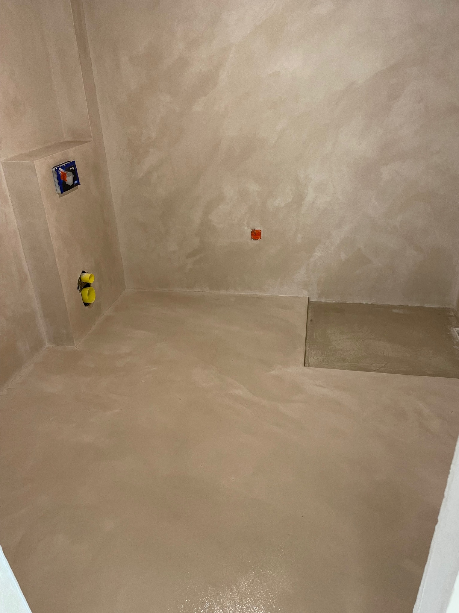 Beżowa łazienka z mikrocementu z widocznymi instalacjami hydraulicznymi i elektrycznymi przed montażem armatury.