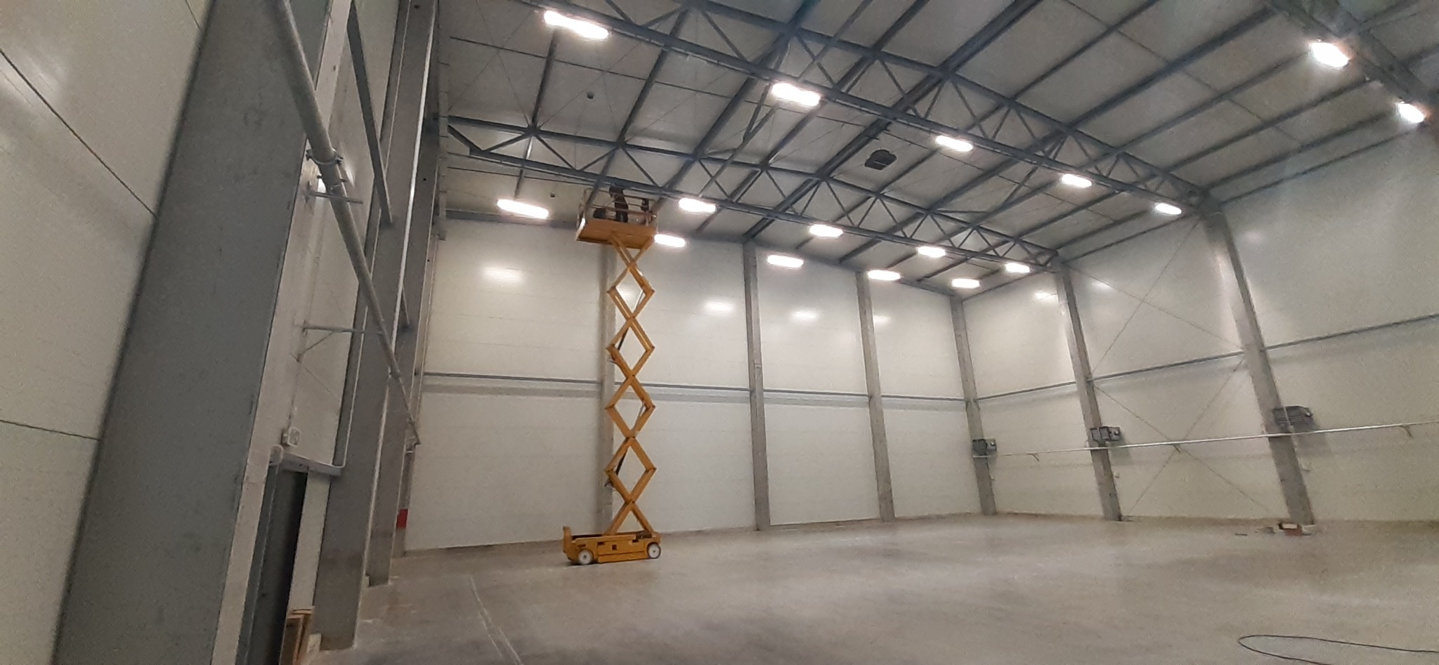 Wysięgnik koszowy wewnątrz hali magazynowej podczas montażu oświetlenia sufitowego LED.