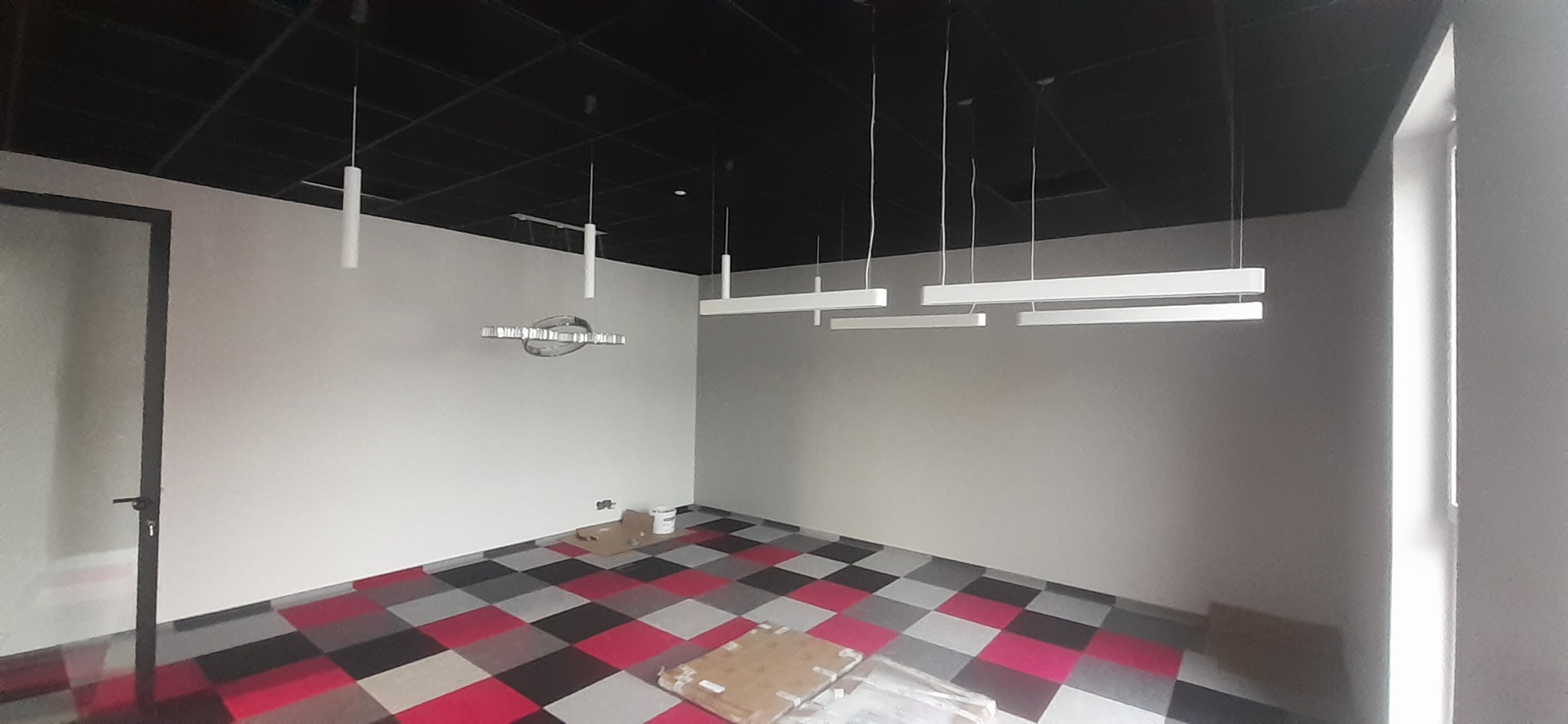 Wnętrze biurowe z zamontowanym oświetleniem: podwieszany sufit, szachownica na podłodze i kilka rodzajów lamp