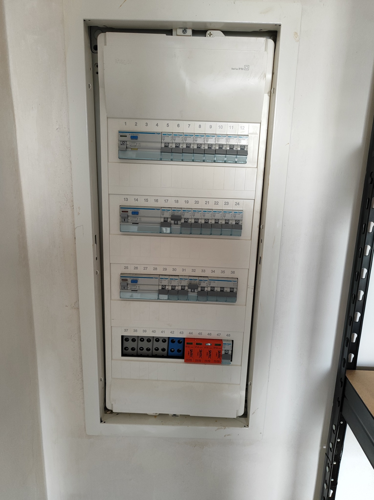 Rozdzielnica elektryczna z bezpiecznikami i zabezpieczeniami przepięciowymi, zamontowana w ścianie wnęki. Widoczne oznaczenia numeracji obwodów od 1 do 48.