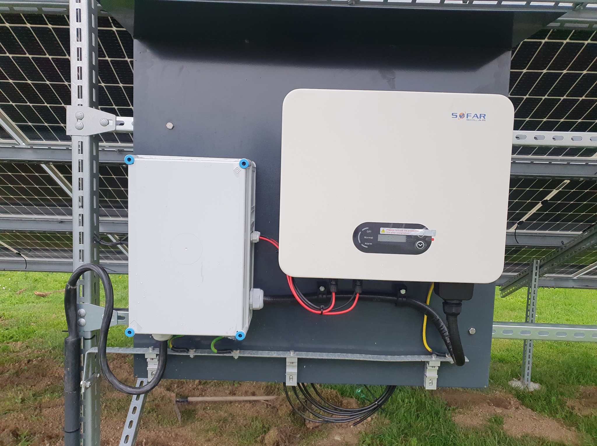 Biały inwerter Sofar Solar zamontowany na konstrukcji paneli słonecznych, z widoczną skrzynką przyłączeniową i okablowaniem na tle zielonej trawy.