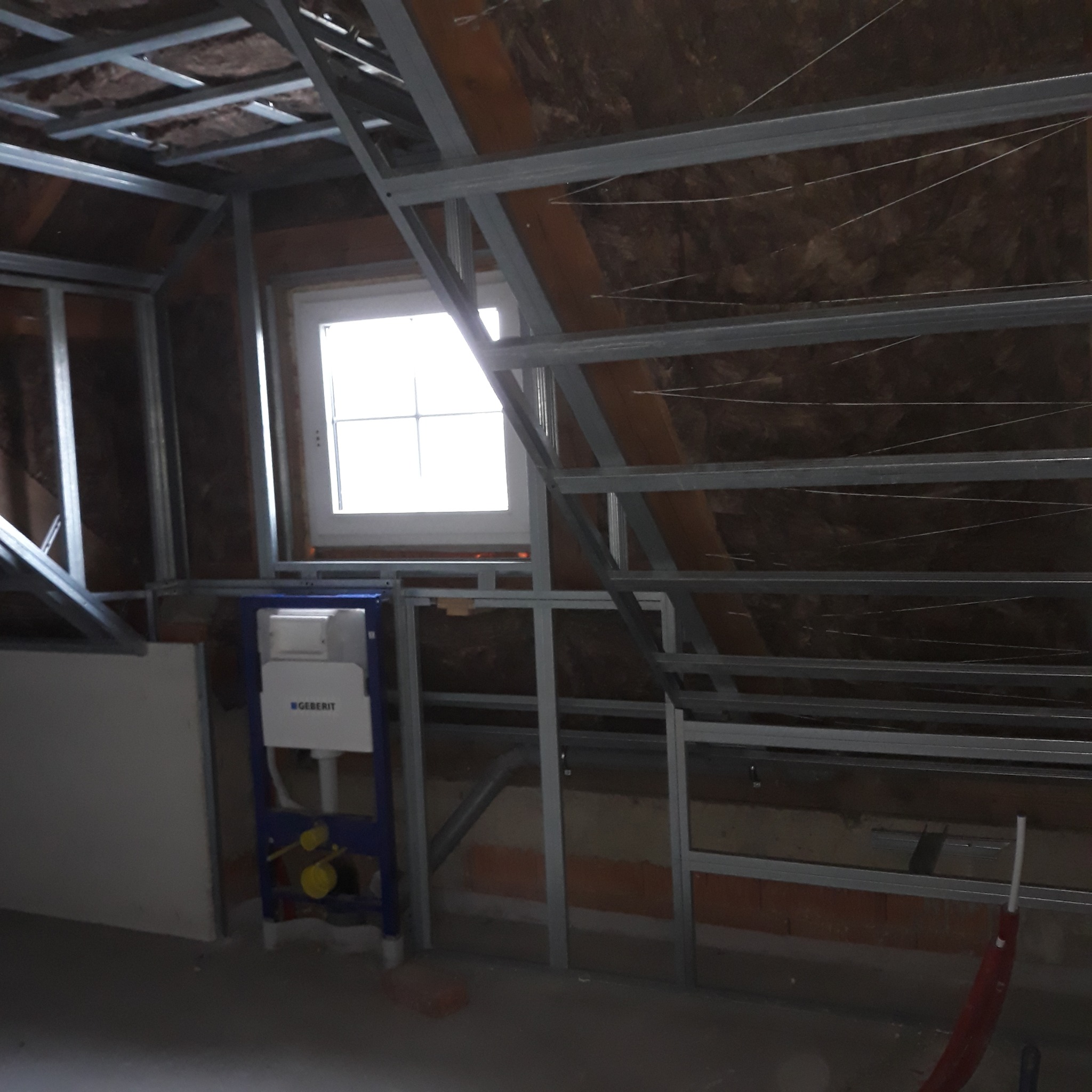 Stelaż metalowy pod zabudowę poddasza z oknem i instalacją sanitarną Geberit. Widoczne ocieplenie wełną mineralną. Etap prac wykończeniowych.