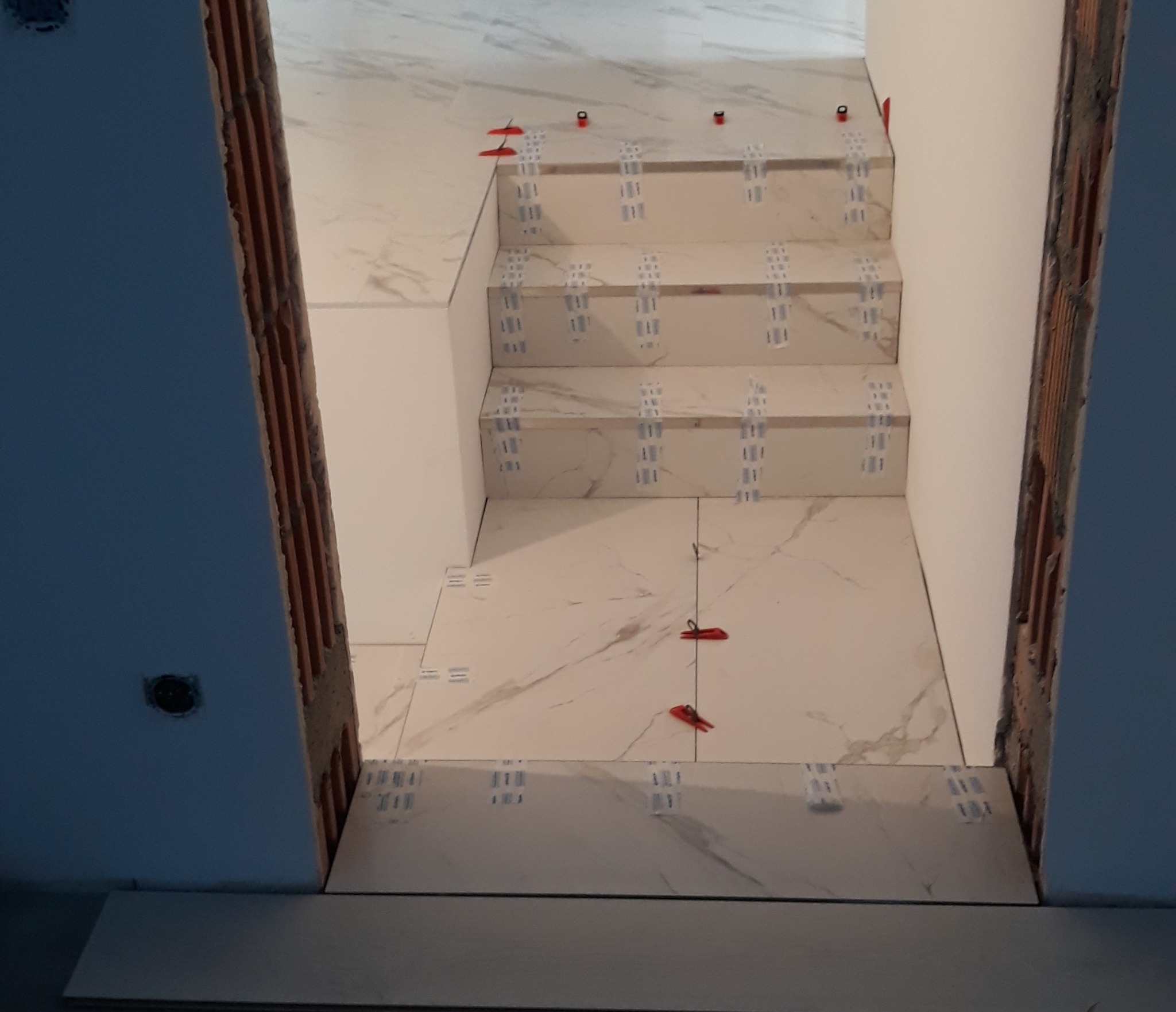 Układanie marmurowych płytek na schodach z użyciem klipsów poziomujących. Widok z góry na etapie prac wykończeniowych. Ściany w surowym stanie.