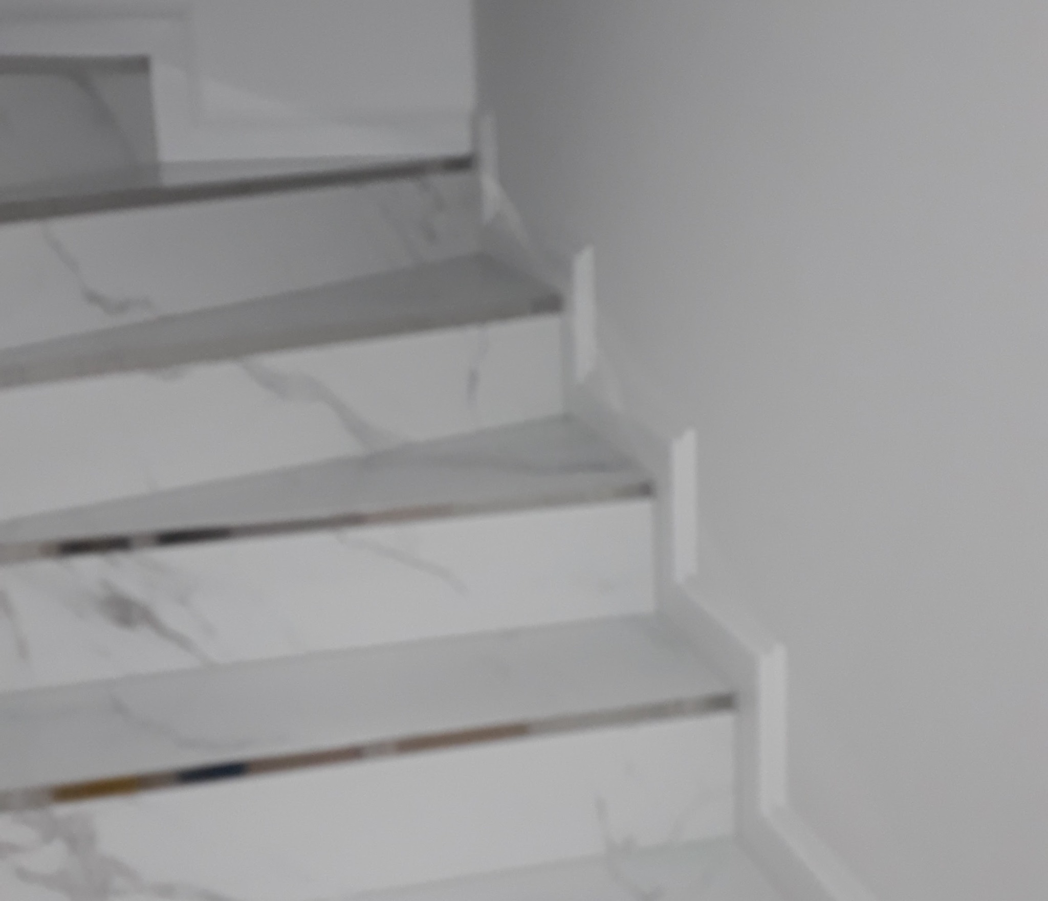 Białe schody z marmurowym wzorem, wykończone listwami, przylegające do białej ściany. Ujęcie z góry, prezentujące detale wykończenia.