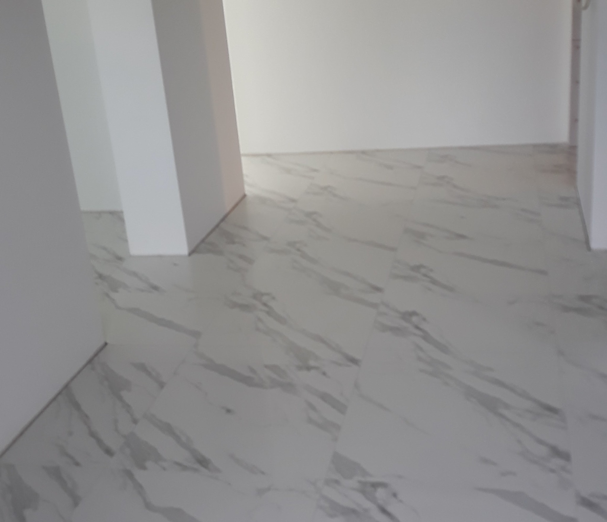 Jasna, marmurowa podłoga w nowym, minimalistycznym wnętrzu. Widoczne białe ściany i filary. Delikatny wzór na płytkach dodaje elegancji. Ukończona realizacja.