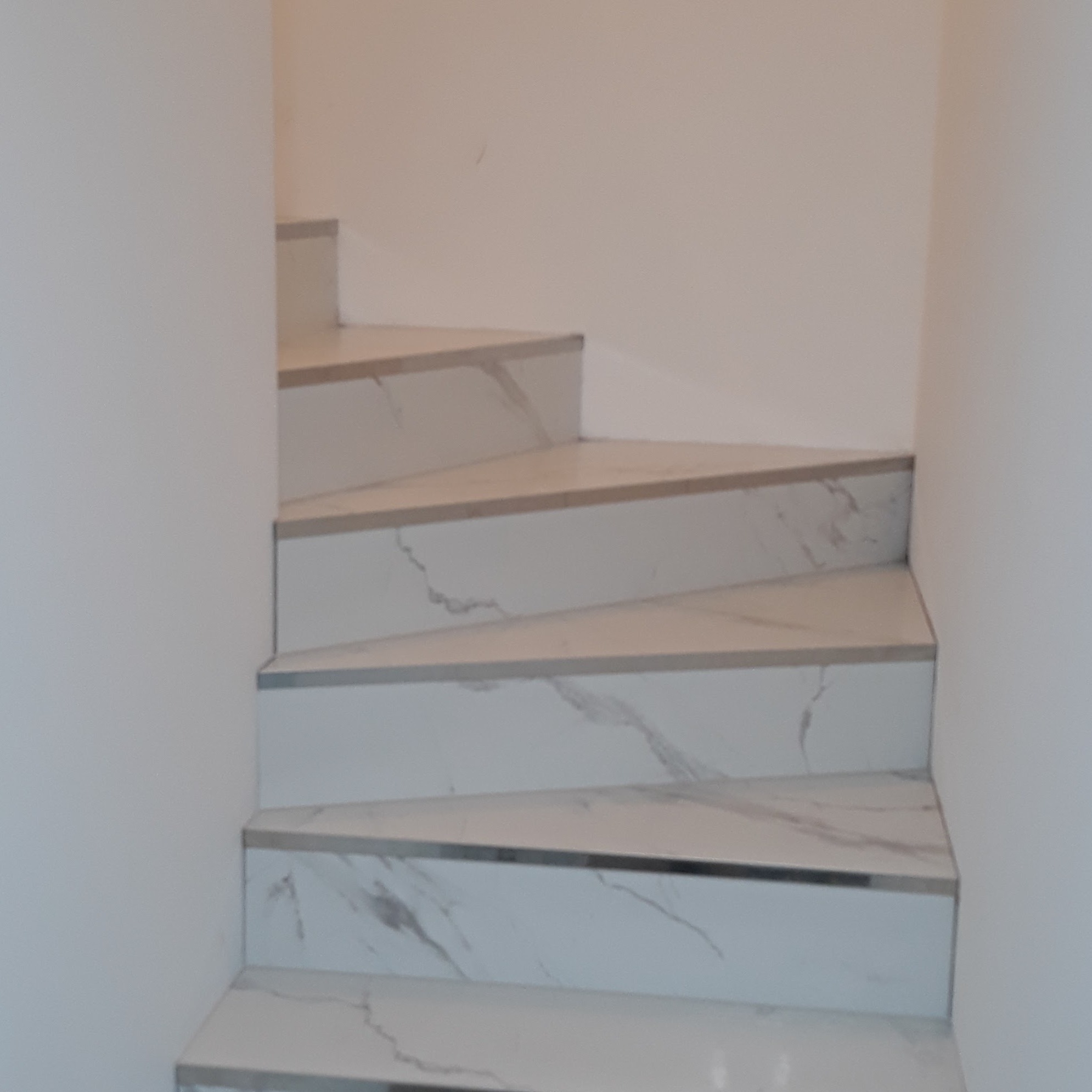 Wykończone schody z białego marmuru z szarymi żyłkami, prowadzące w górę. Widoczne detale wykończenia krawędzi. Minimalistyczny design w jasnym wnętrzu.