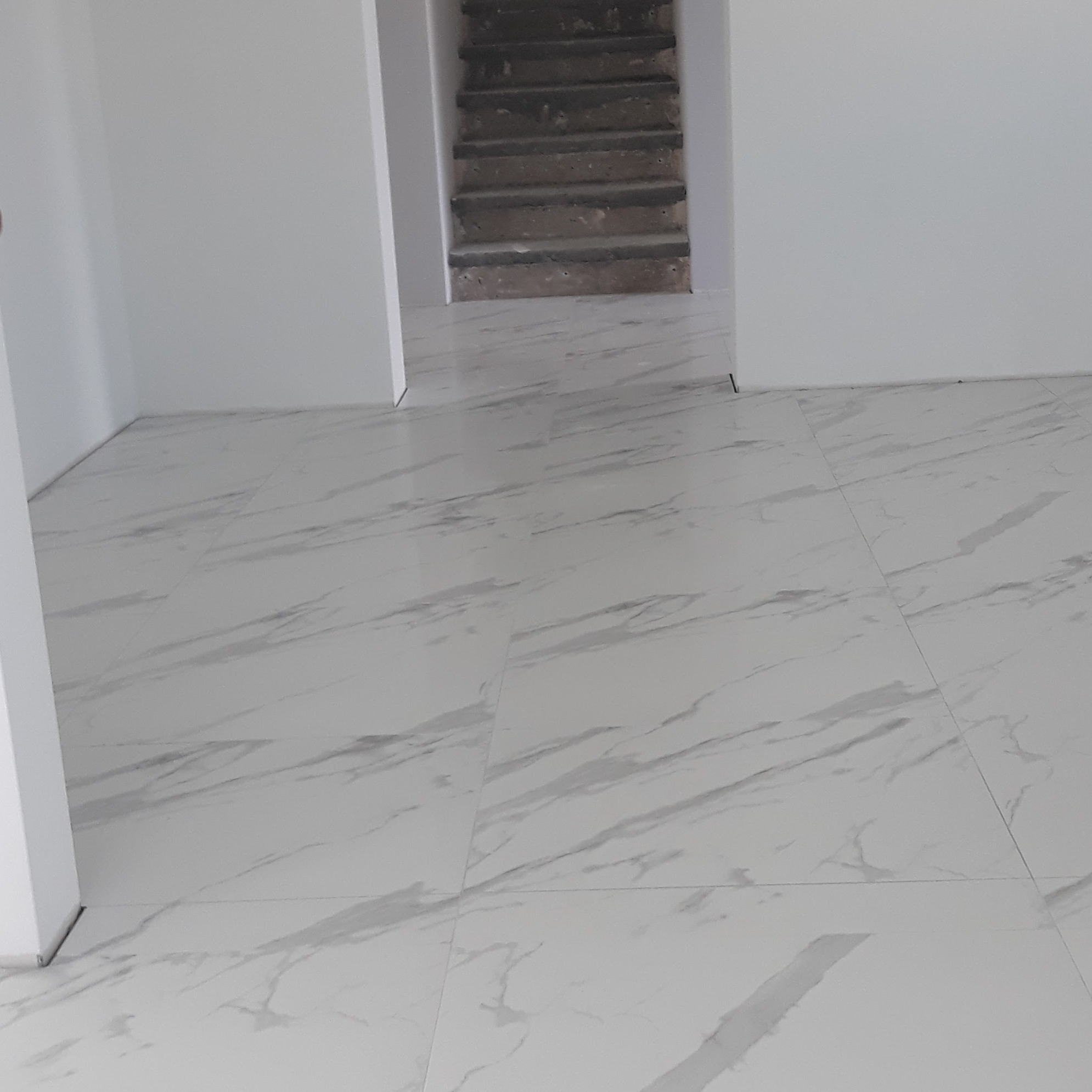 Biała podłoga z płytek imitujących marmur w jasnym wnętrzu. W tle widoczne schody. Minimalistyczny design, czyste linie, świeżo położona podłoga.