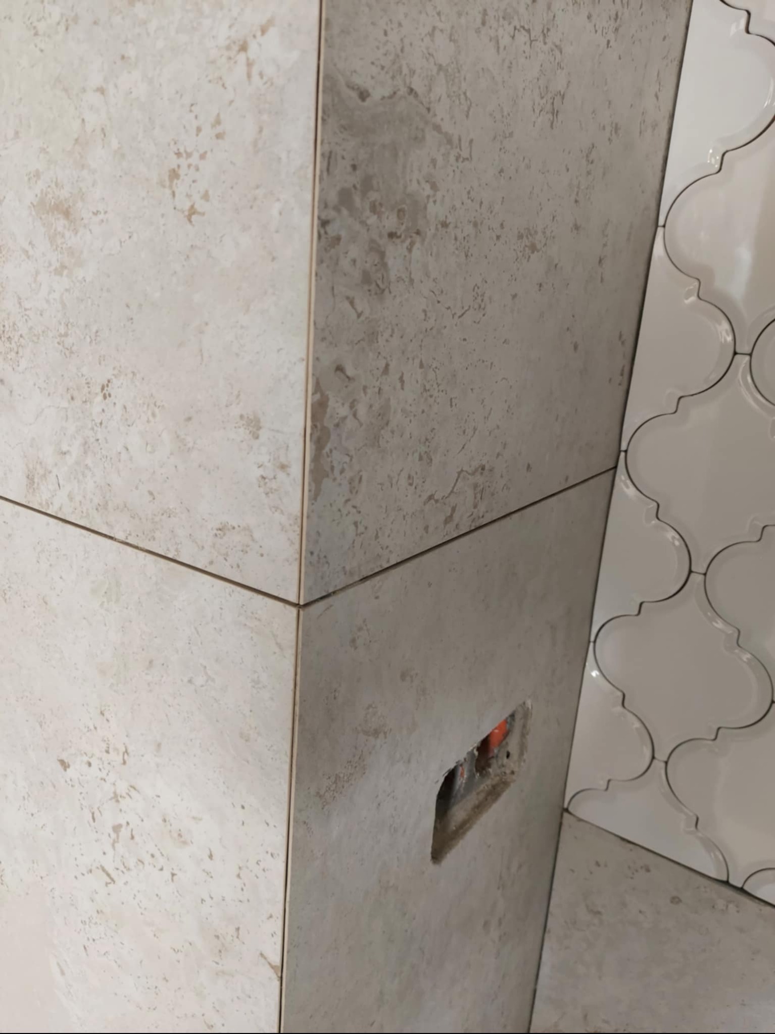 Beżowe płytki imitujące kamień na ścianie, z wyciętym otworem na instalację. Obok białe, dekoracyjne płytki w marokański wzór. Detal wykończenia.