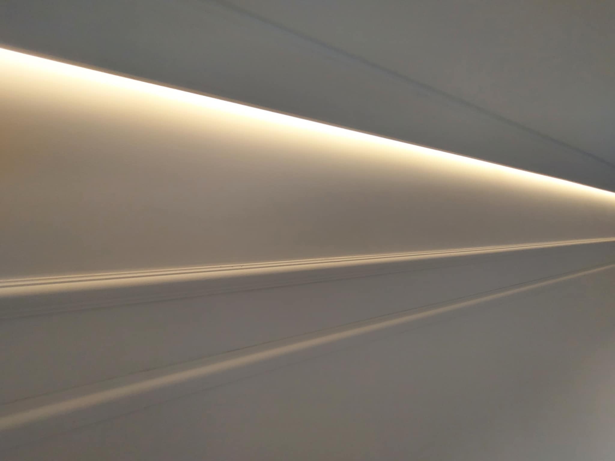 Biały sufit z subtelnym oświetleniem LED wzdłuż krawędzi, tworzącym nowoczesny i minimalistyczny efekt wizualny. Delikatne cienie podkreślają strukturę.