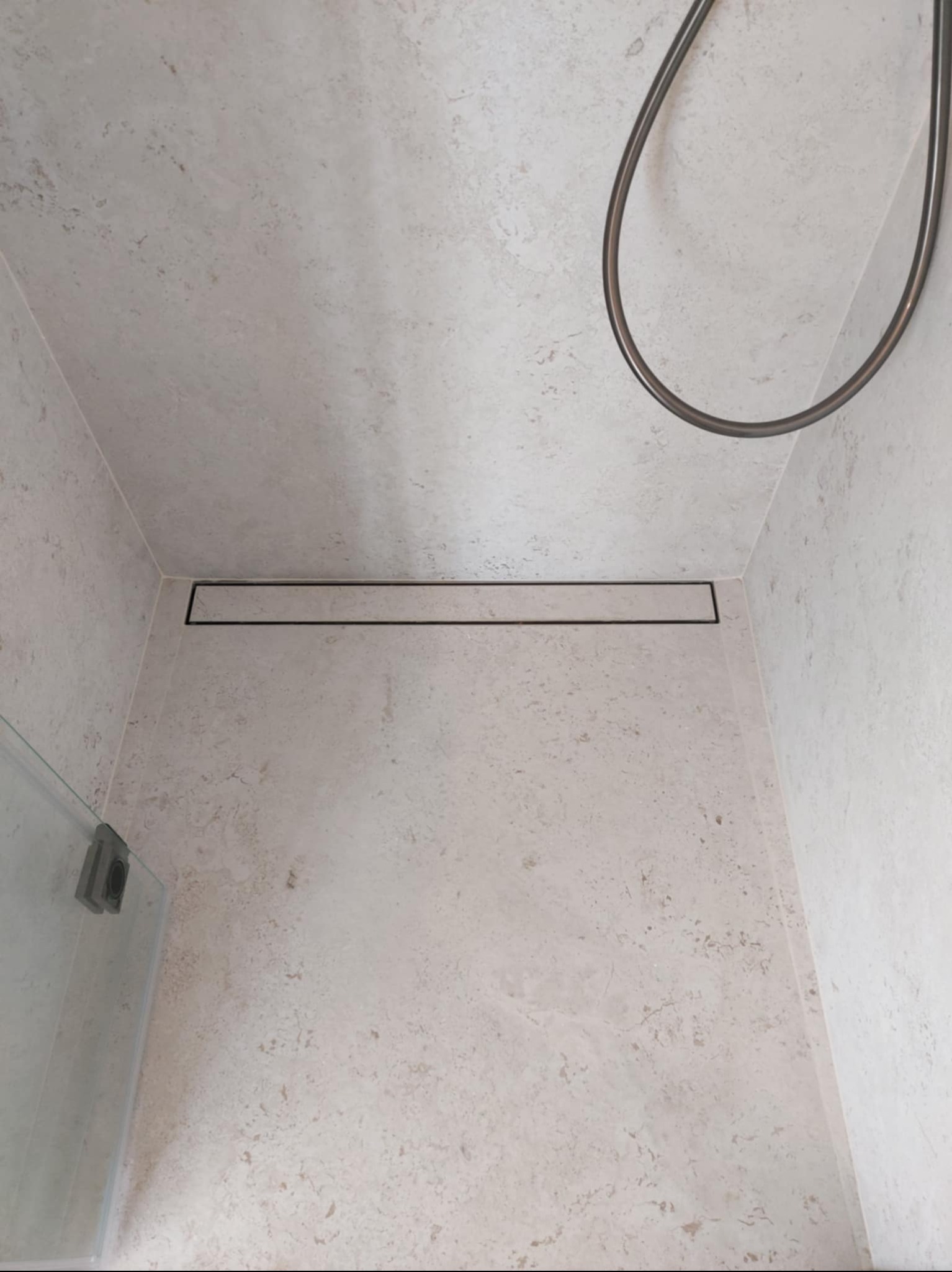 Beżowa łazienka z odpływem liniowym i deszczownicą. Płytki imitujące kamień na ścianach i podłodze. Minimalistyczny design.