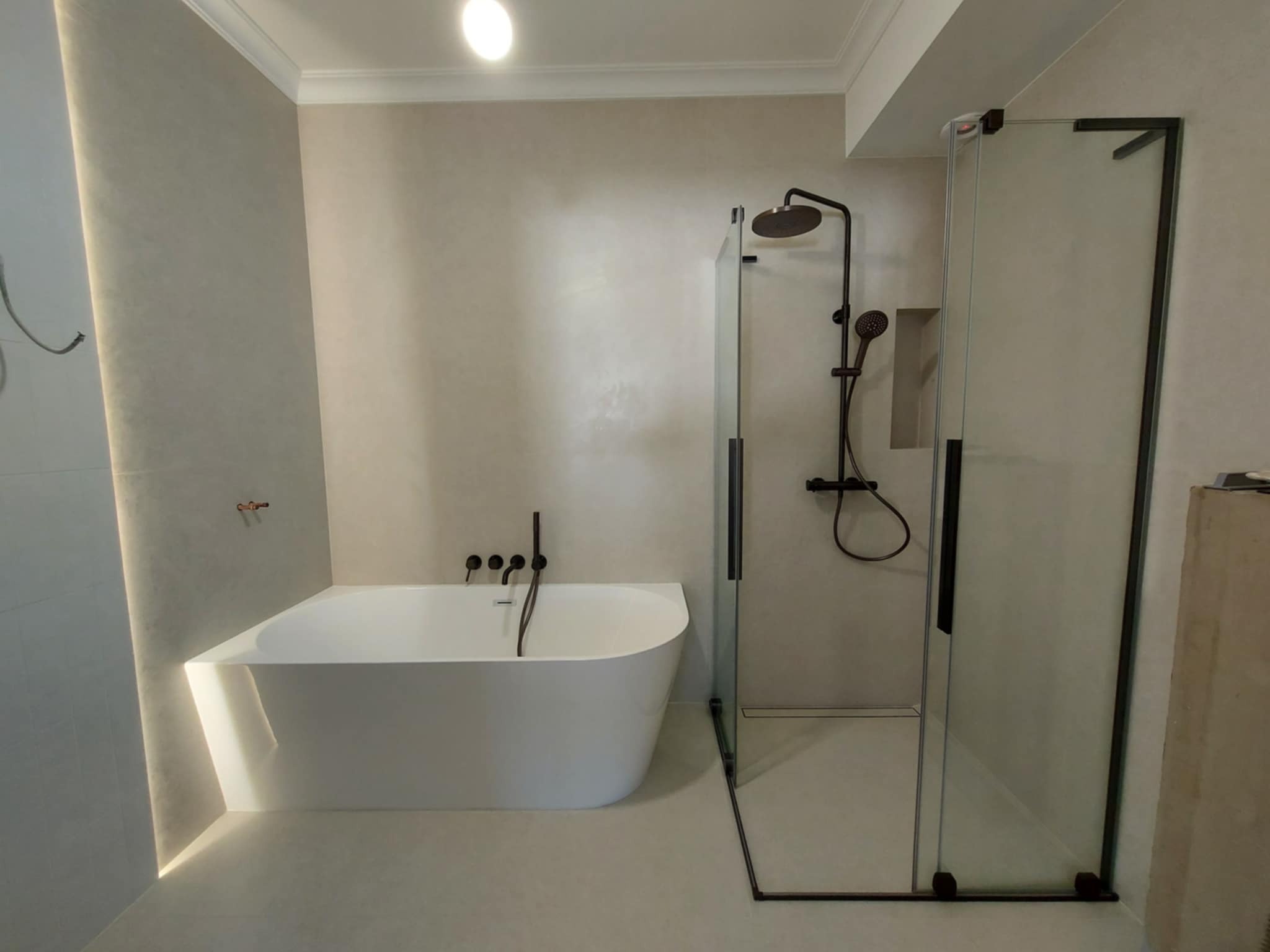 Nowoczesna łazienka w beżach: wolnostojąca wanna, kabina prysznicowa typu walk-in z czarnymi detalami, minimalistyczna armatura i subtelne oświetlenie.