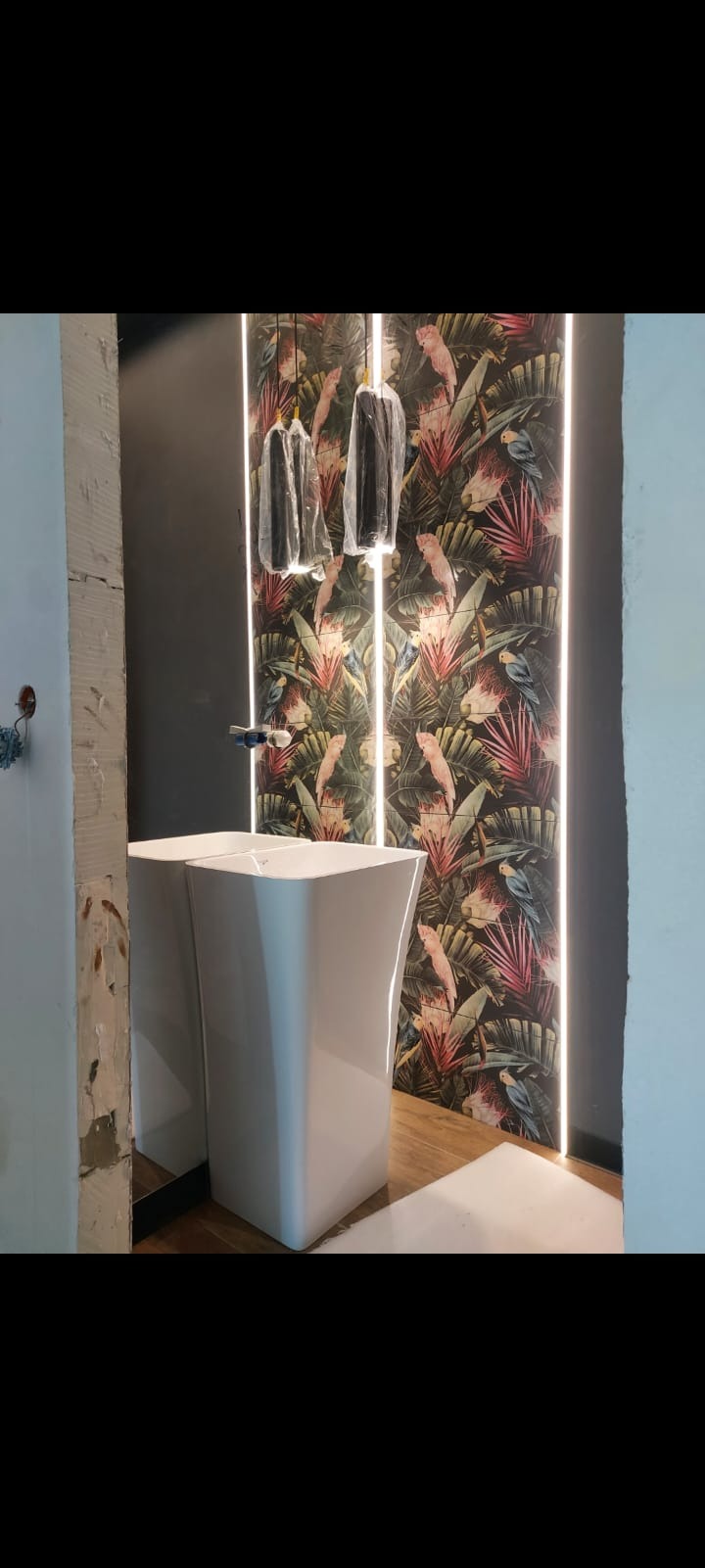 Nowoczesna łazienka w trakcie wykończenia: biała umywalka wolnostojąca, ściana z motywem tropikalnym i oświetleniem LED. Widoczne elementy instalacji.