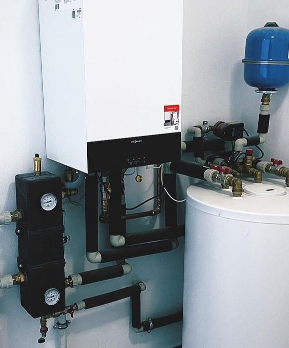 Kompaktowa kotłownia z białym kotłem wiszącym Viessmann, zbiornikiem akumulacyjnym i rozbudowanym systemem rur miedzianych z czarną izolacją, manometry na czarnym rozdzielaczu, niebieskie naczynie...