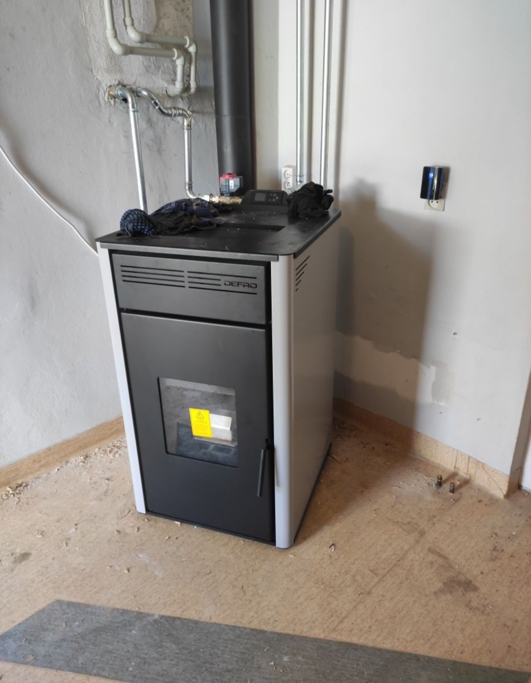 Nowoczesny piec na pellet marki Defro w kotłowni, widoczne rury instalacji grzewczej i przewód kominowy.