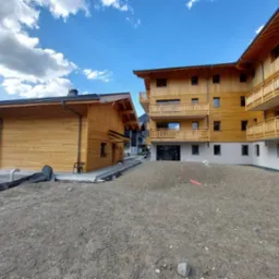 Nowo wybudowany, drewniany budynek mieszkalny z balkonami, widok z zewnątrz na plac budowy z hałdą ziemi.