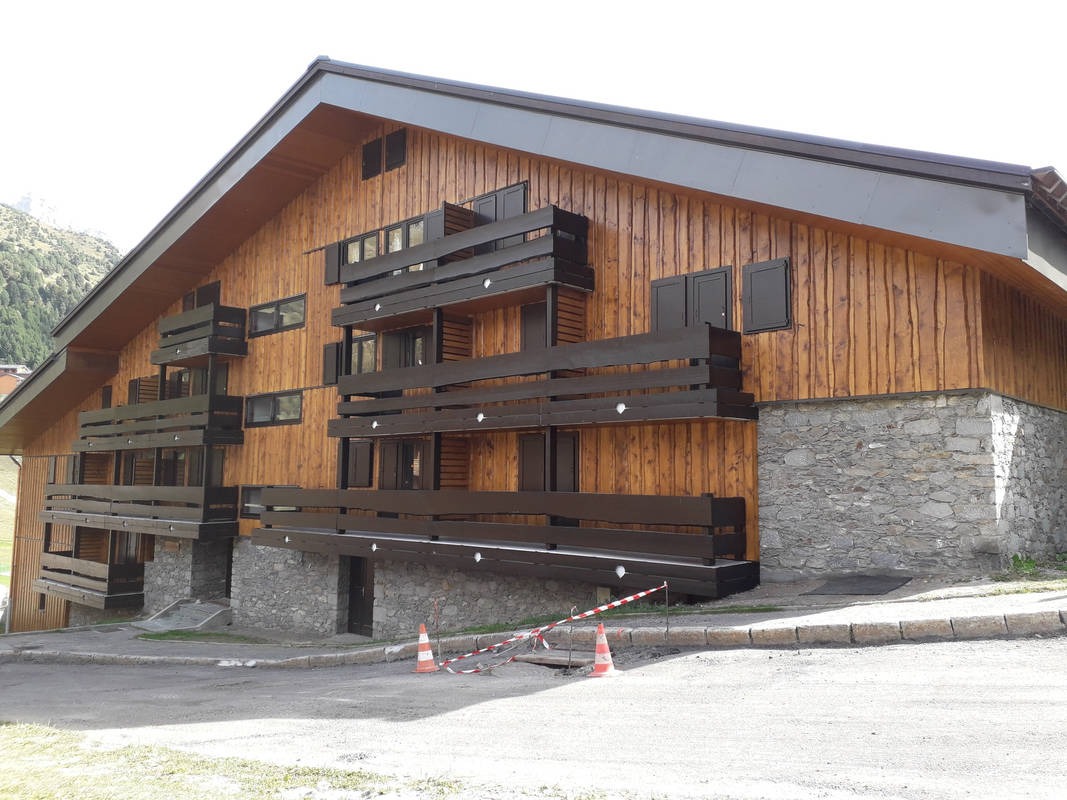 Drewniany budynek z ciemnym dachem i balkonami, zabezpieczone miejsce na zewnątrz, góry w tle.