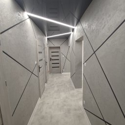 Aleksandra Szempruch - Korytarz po remoncie w odcieniach szarości z gładzią na ścianach, czarnymi geometrycznymi wzorami, podwieszanym, lustrzanym sufitem z ledowym oświetleniem i trzema parami drzwi. Podłoga wyłożona...