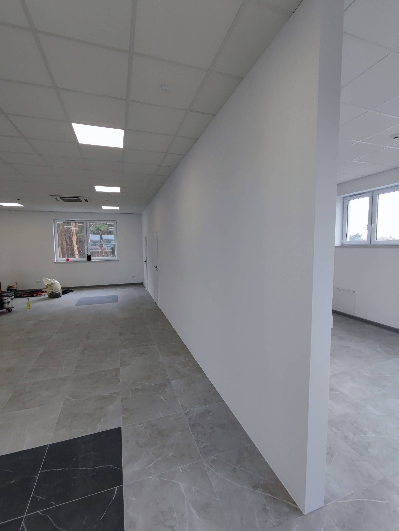 Wnętrze wykończonego biura z gładkimi, białymi ścianami, szarą podłogą z płytek imitujących marmur i sufitem kasetonowym z oświetleniem LED.