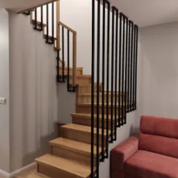 Drewniane schody z czarną, pionową balustradą w nowoczesnym wnętrzu, obok stoi sofa w odcieniu brudnego różu.