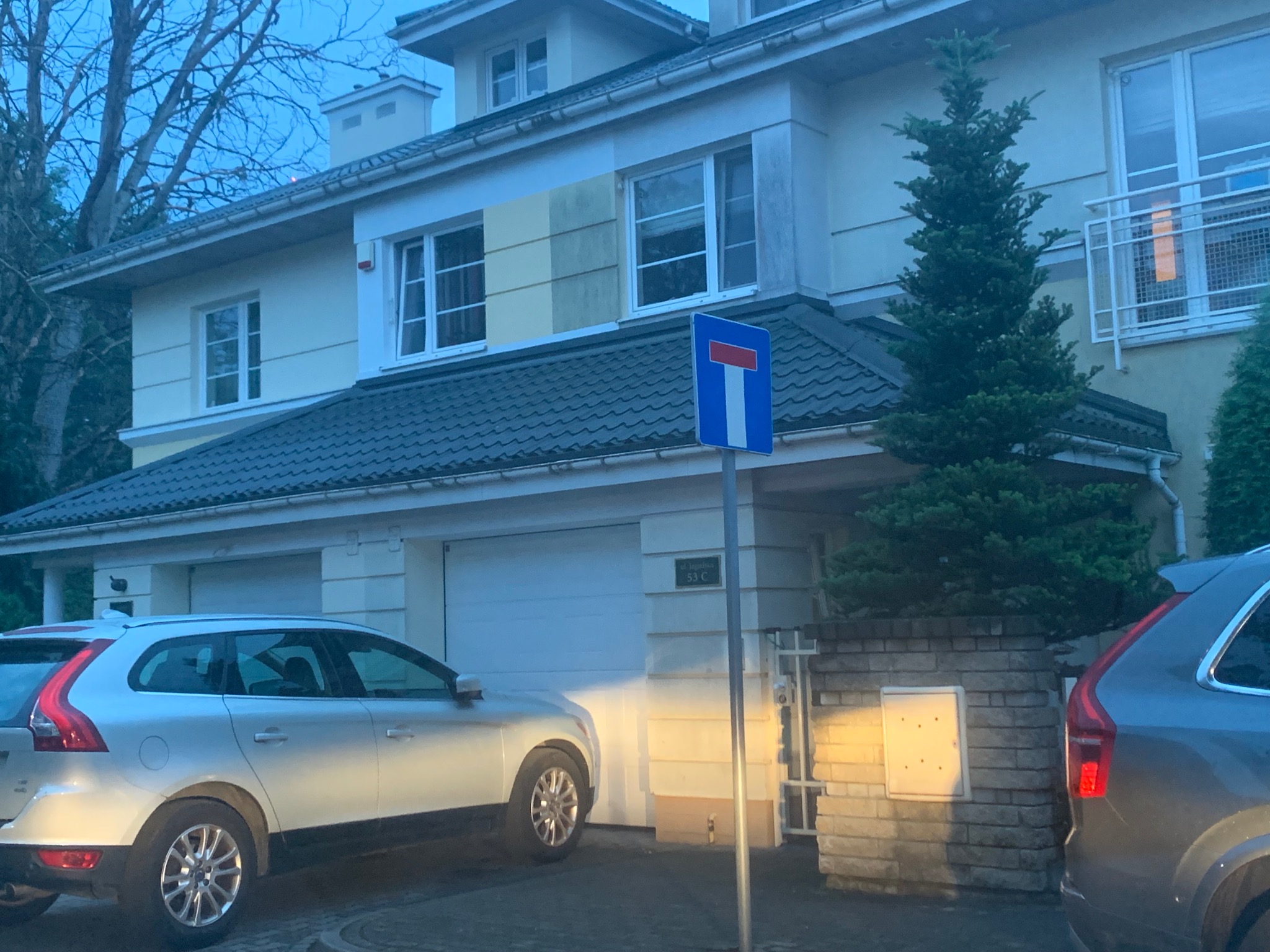 Dwupiętrowy dom z garażem i fragmentem elewacji z próbkami kolorów, widoczny znak drogowy T-27.