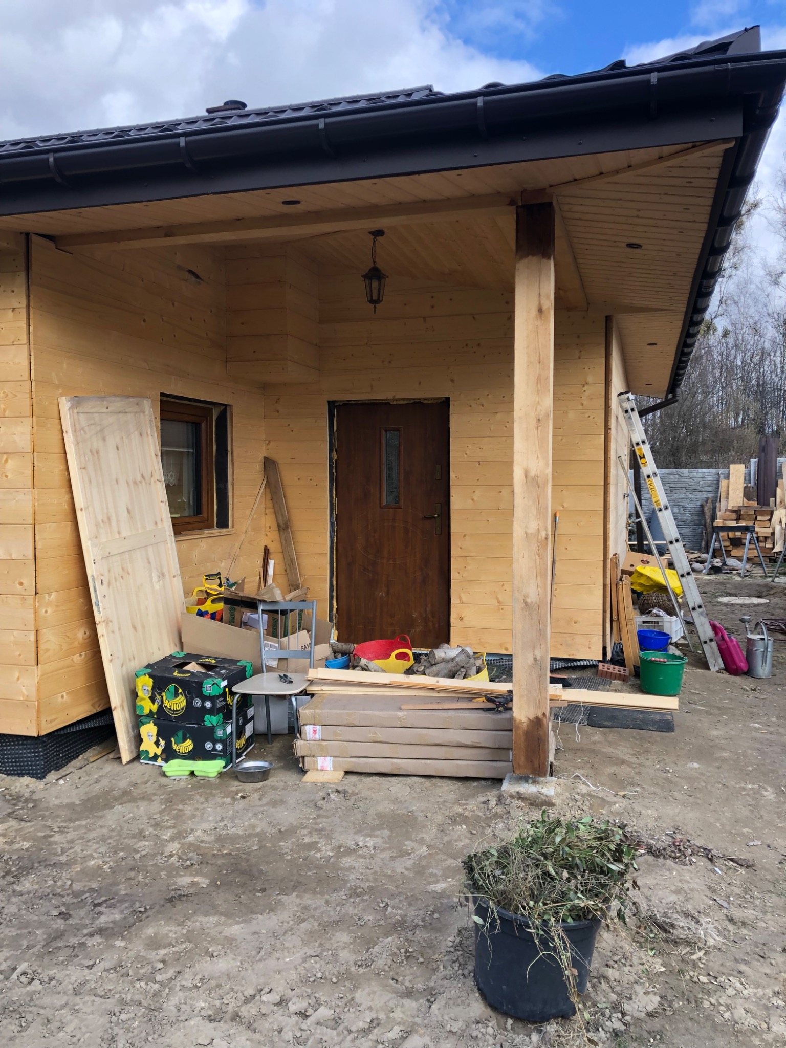 Wznoszenie drewnianego domu: widok na częściowo wykończony budynek z widoczną konstrukcją, drewnianymi panelami i elementami wykończeniowymi, z materiałami budowlanymi i narzędziami rozłożonymi...