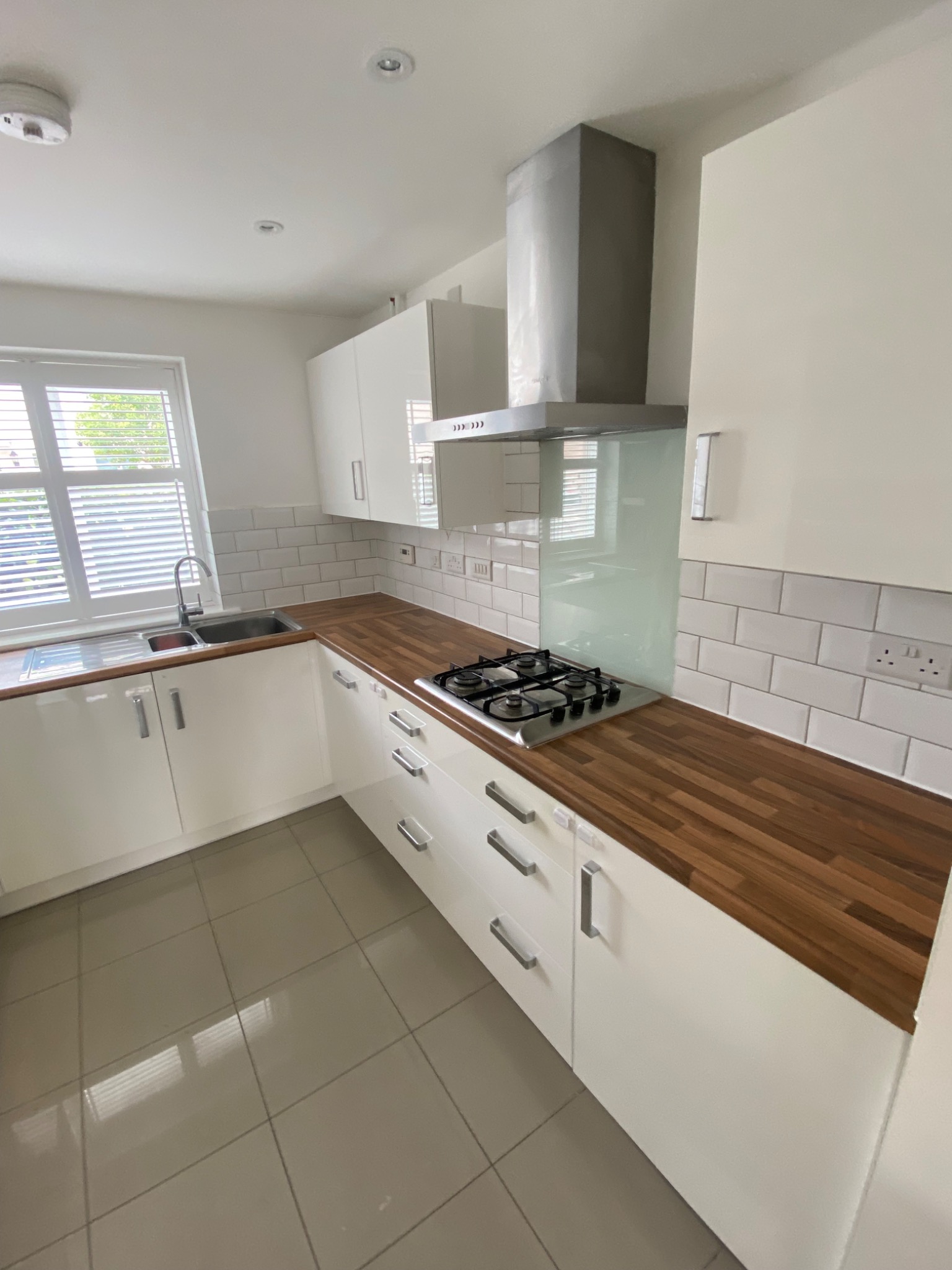 Jasna kuchnia z drewnianym blatem, białymi szafkami i płytkami w stylu metro, okap ze stali nierdzewnej i widok na zewnątrz przez okno.